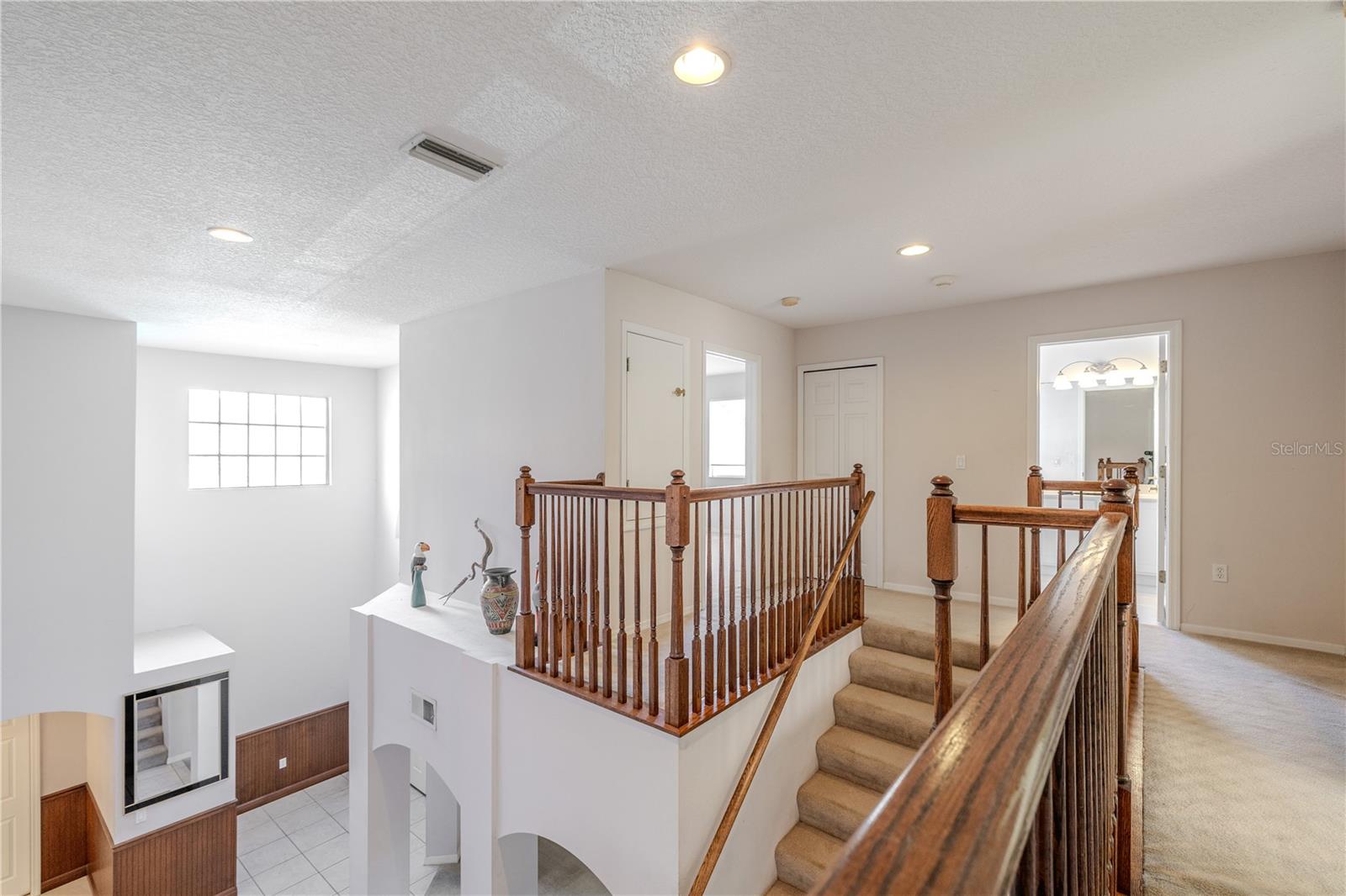 Open upstairs landing overlooks the dramatic two-story foyer and features warm wood railings, creating a bright, airy connection between bedrooms and baths.
