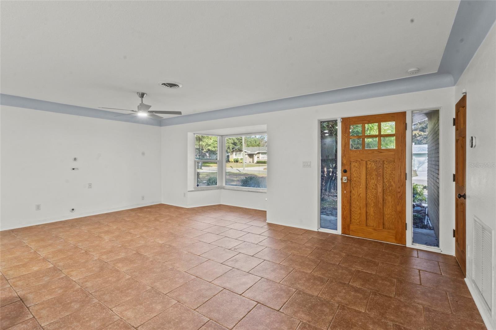 Spacious living room with large front windows, modern ceiling fan, and abundant natural light.