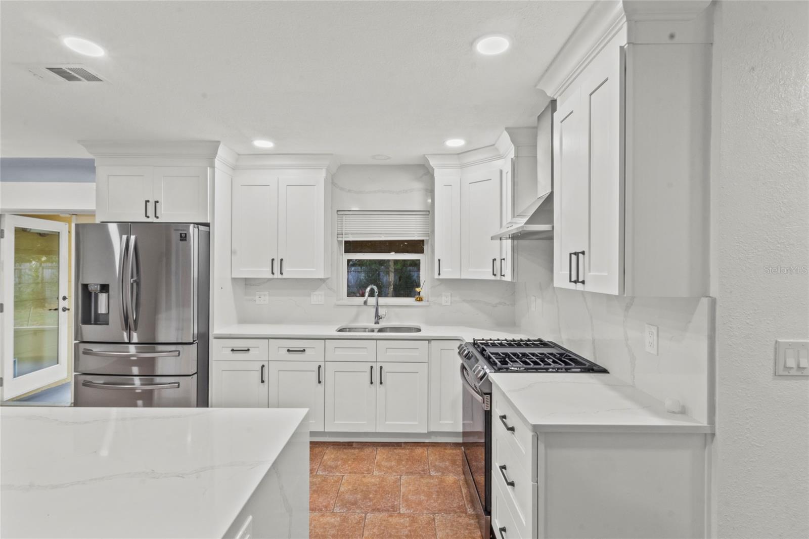 Stylish kitchen showcasing stainless-steel gas range, designer hood, custom cabinetry, and elegant stone countertops.