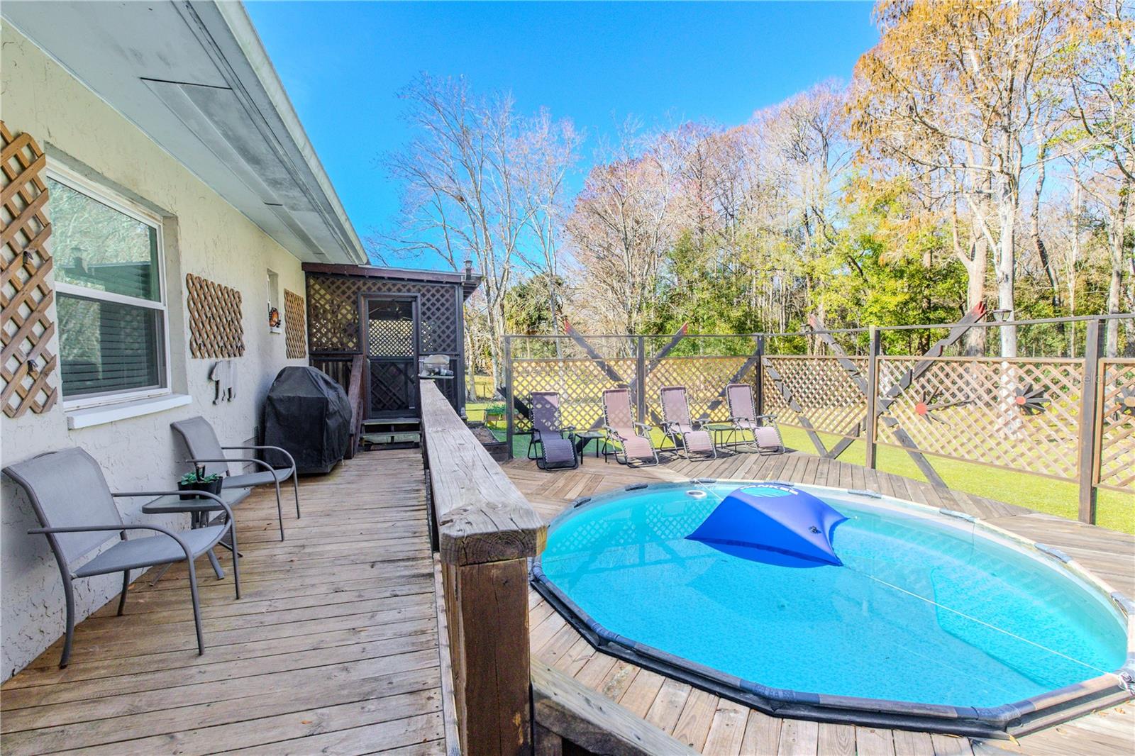 A wide exterior walkway connects the main deck areas, providing easy access between the pool and the home. Wood railings and lattice details add continuity, while the elevated design enhances flow and usability.