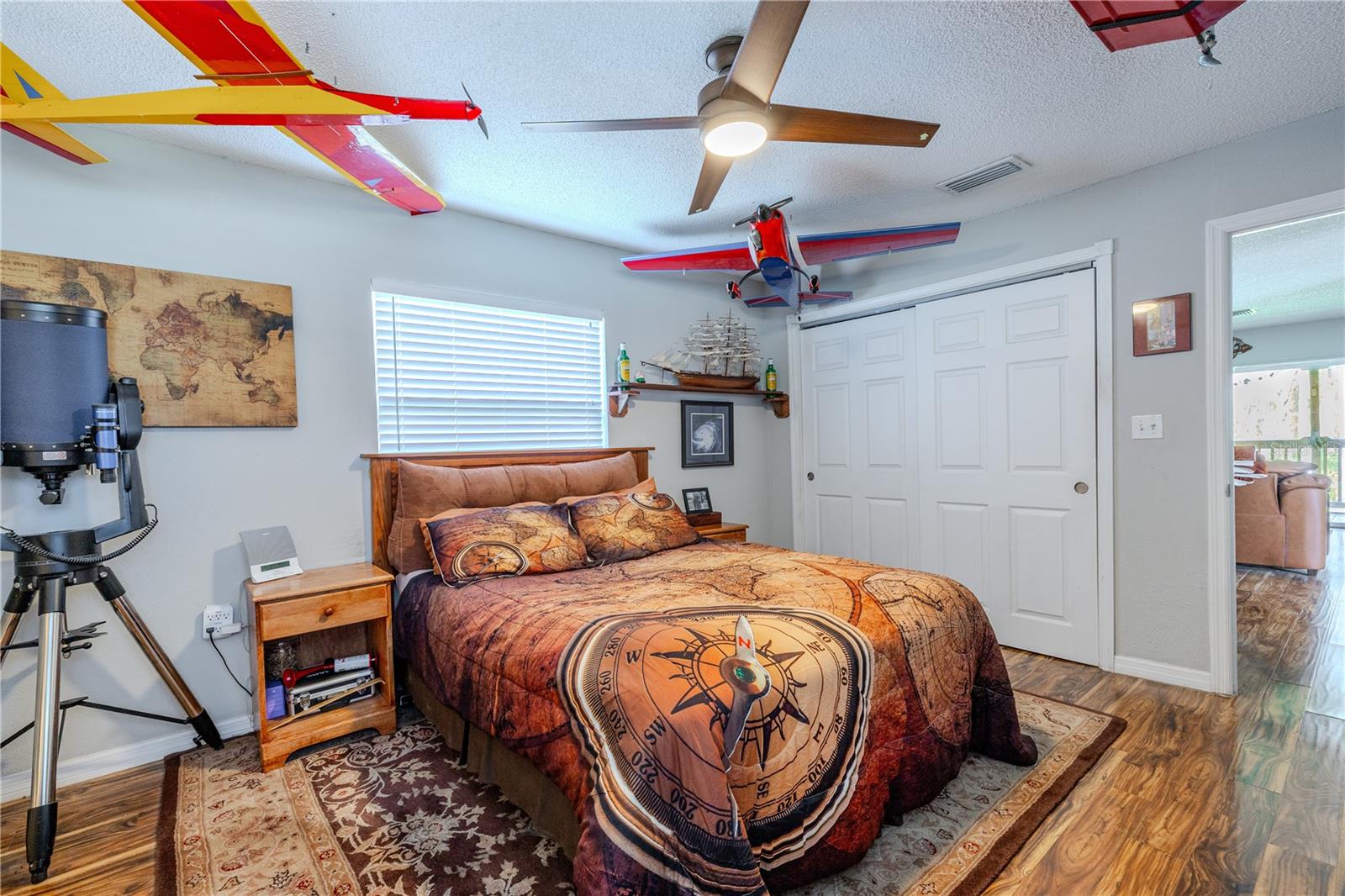 Comfortable primary bedroom with laminate flooring continuing throughout and a large window fitted with blinds that filters in natural light while maintaining privacy. The room offers ample wall space for furniture placement and a calm, cohesive feel consistent with the home’s main living areas.