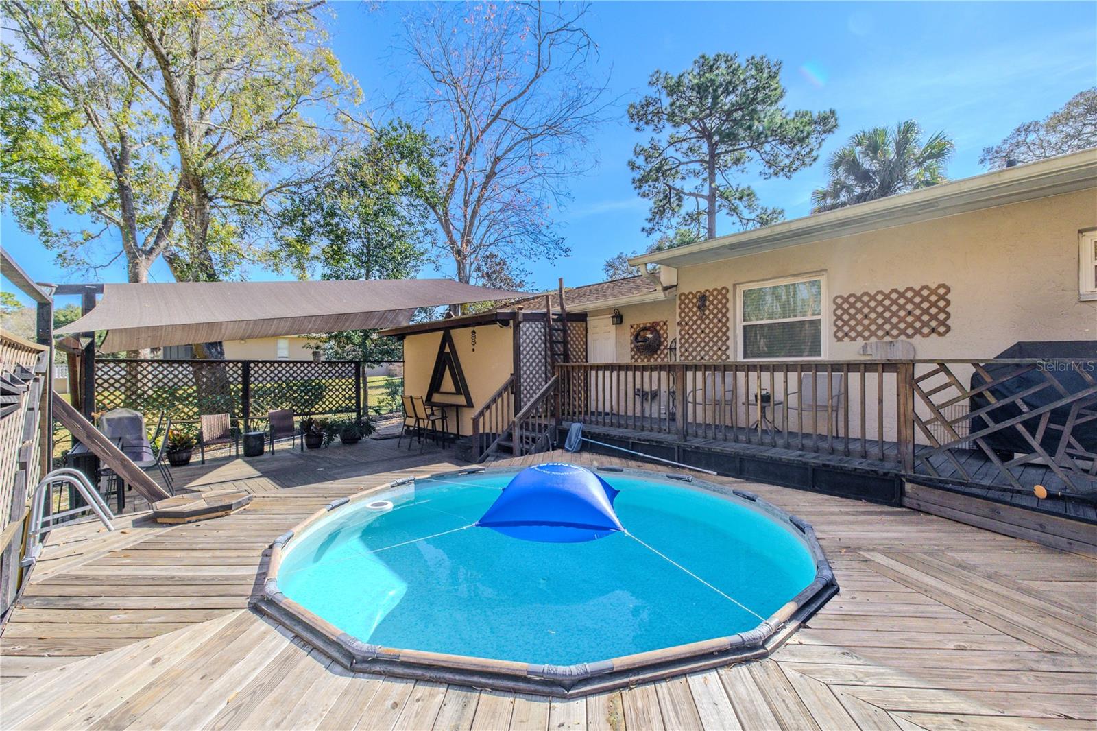 The pool deck serves as the centerpiece of the backyard, offering generous deck space and a semi-enclosed feel created by lattice panels. A shade structure extends the functionality of the outdoor area, making it well-suited for year-round enjoyment.