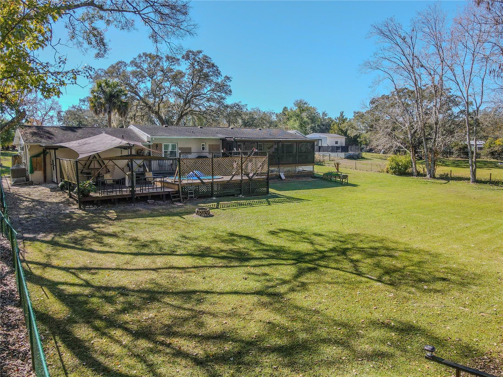 Rear exterior view showing the deck and outdoor living areas set against a broad, grassy yard, with the tree line providing a tranquil, nature-rich backdrop.