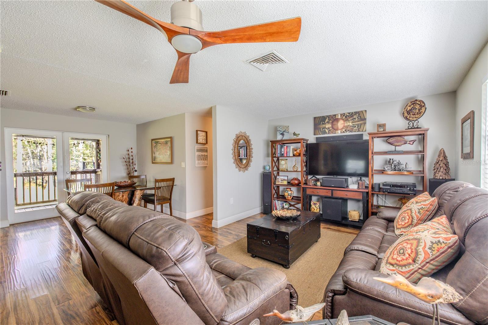 Spacious living room featuring laminate flooring, a ceiling fan, and an open layout that flows easily into the dining area and rear outdoor living space.