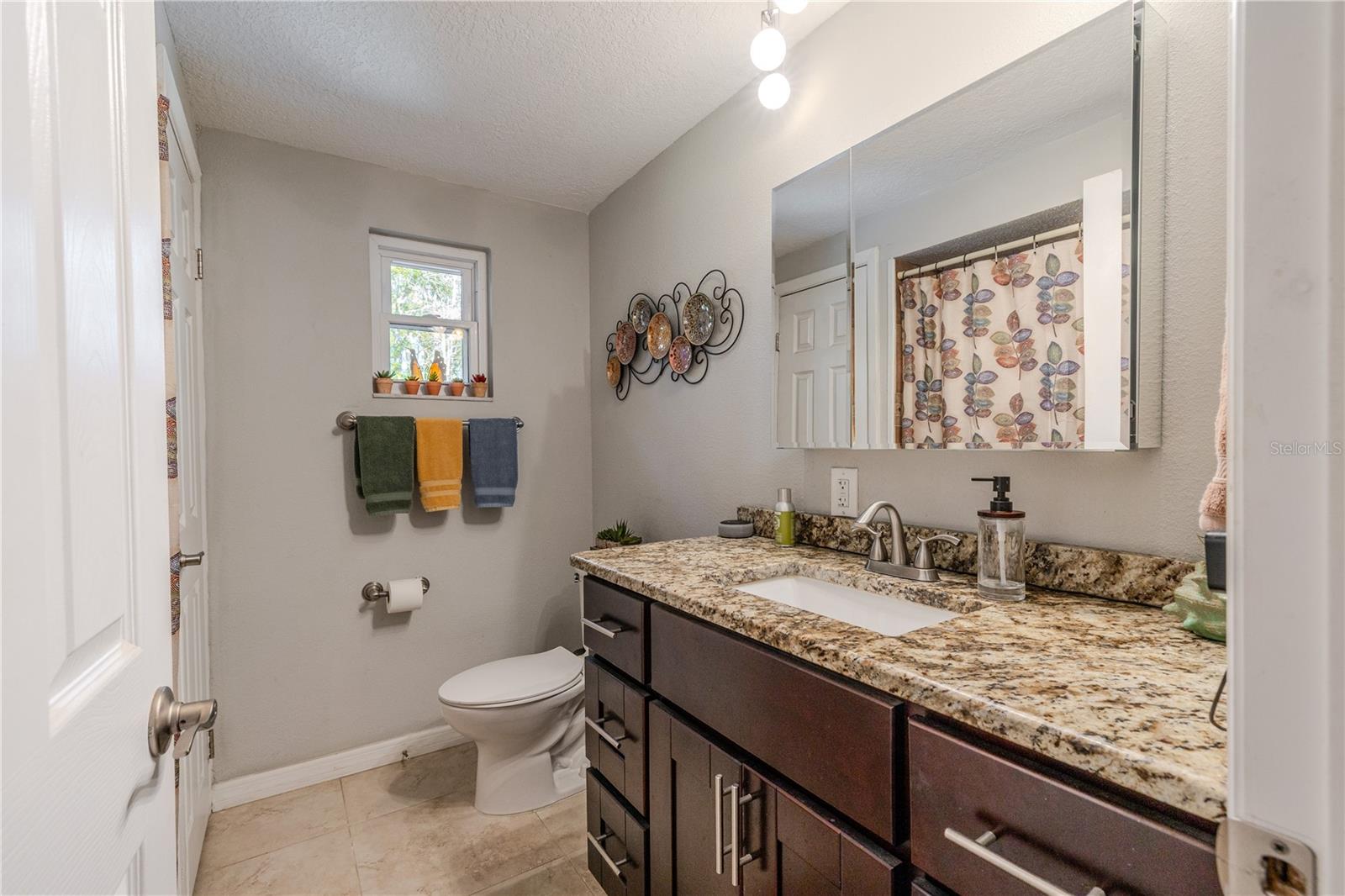 Well-appointed second bath featuring a granite-topped vanity, modern lighting, neutral tile flooring, and a window for natural light.