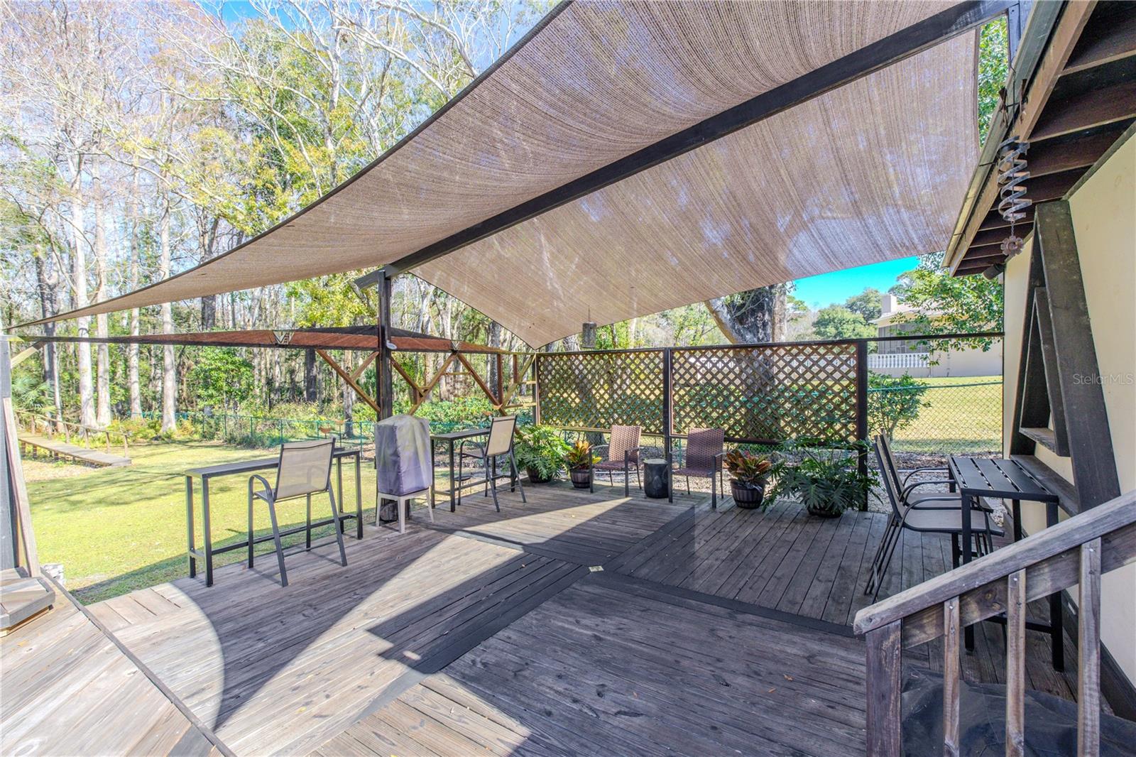 Covered deck with integrated shade sail, wood decking, and lattice accents, creating a defined outdoor living zone with privacy and filtered light.