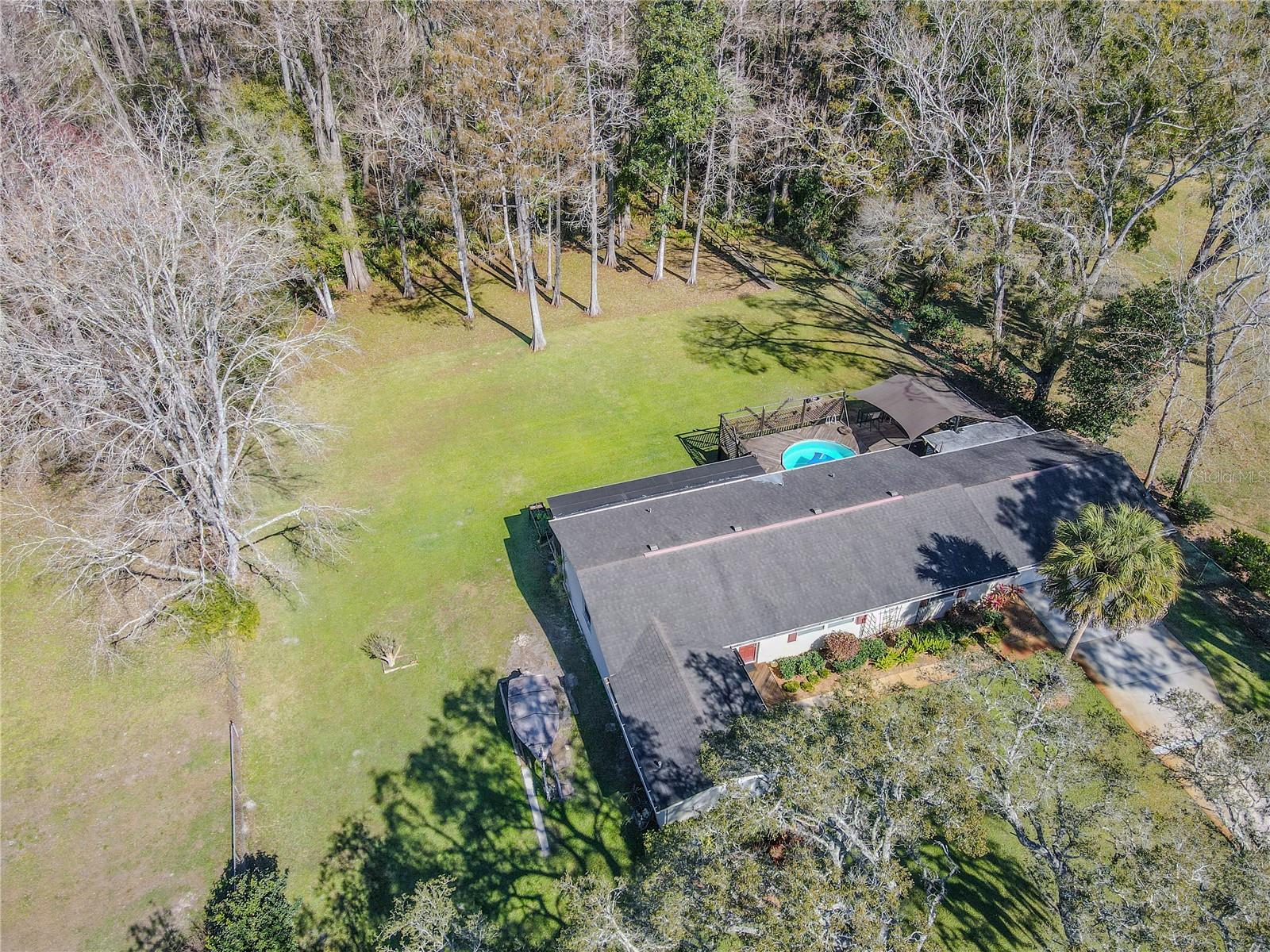 Aerial view showcasing the home’s expansive yard and its relationship to the surrounding woods, highlighting the sense of space and seclusion that defines the setting.