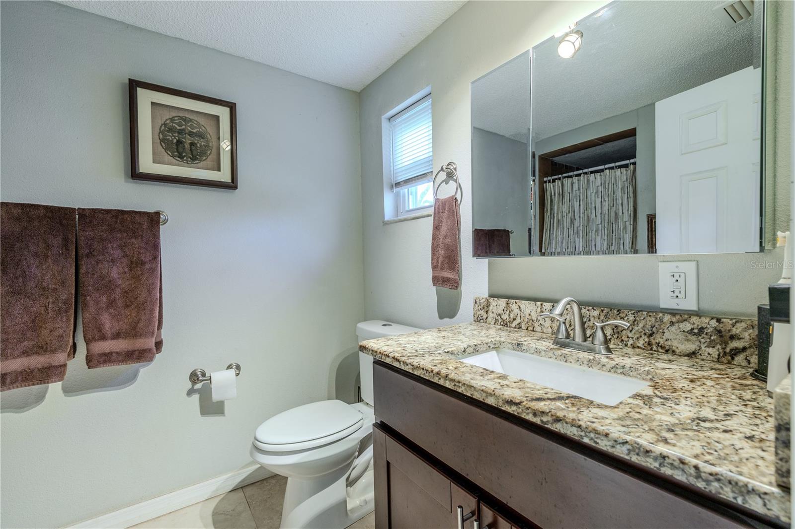 Primary en suite bathroom featuring a granite-topped vanity, undermount sink, brushed-nickel fixtures, and a window providing natural light.