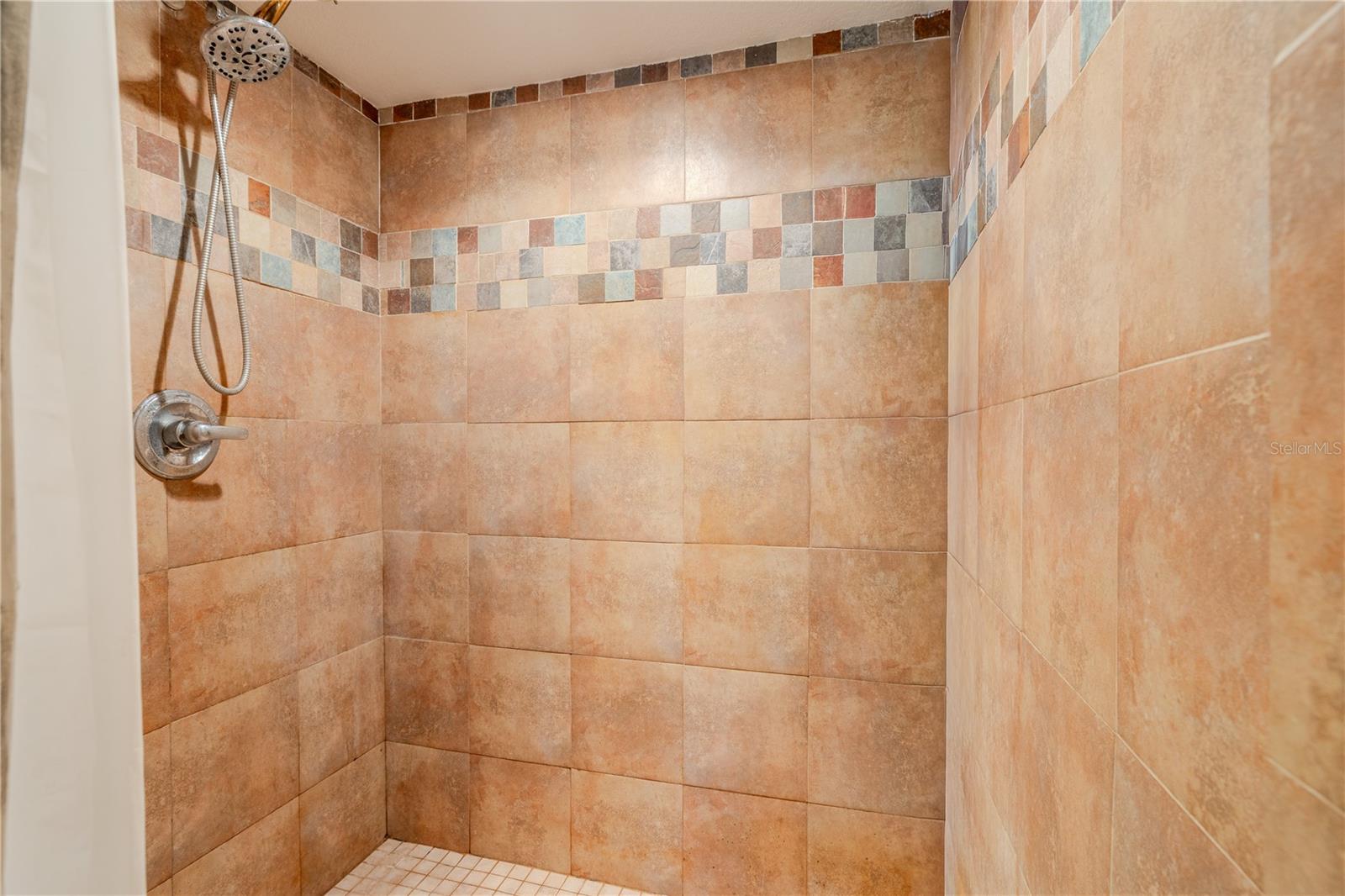 Primary en suite walk-in shower featuring warm-toned tile, mosaic accent detailing, and a spacious, streamlined design.