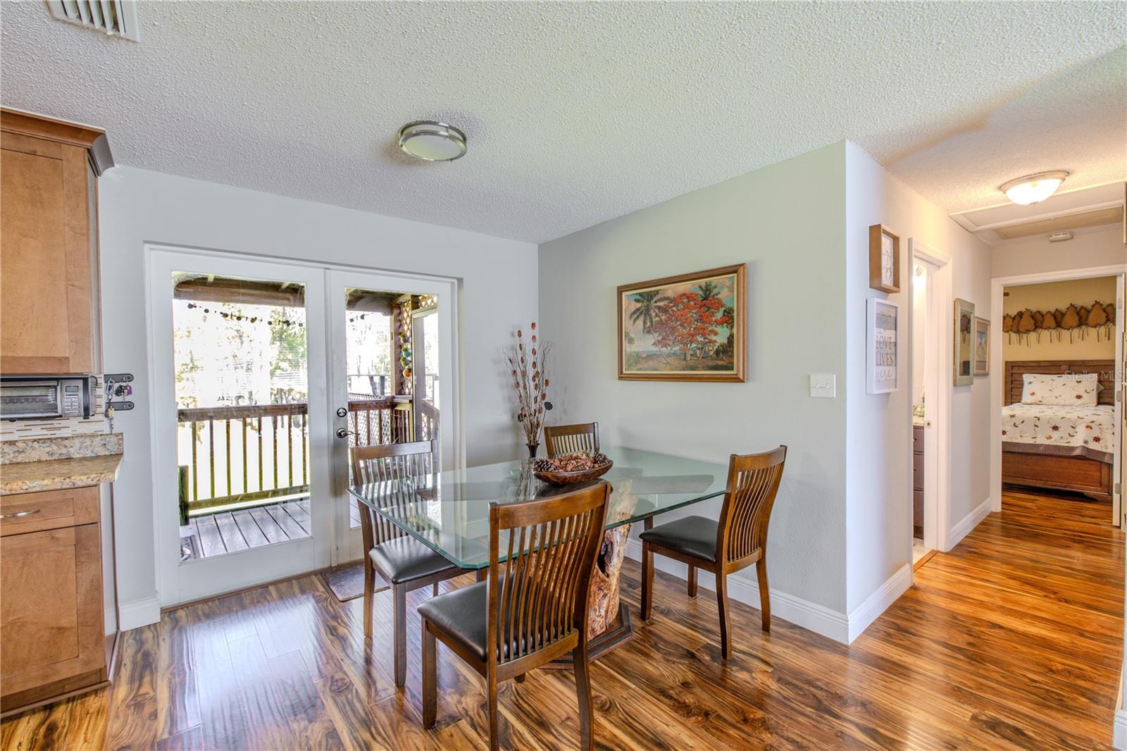 Light-filled dining area surrounded by laminate flooring that continues throughout the main living spaces. Sliding glass doors provide easy access to the covered deck, extending the living space outdoors while offering peaceful, wooded views. Neutral wall tones and clean lines create a versatile setting for casual meals or family gatherings.