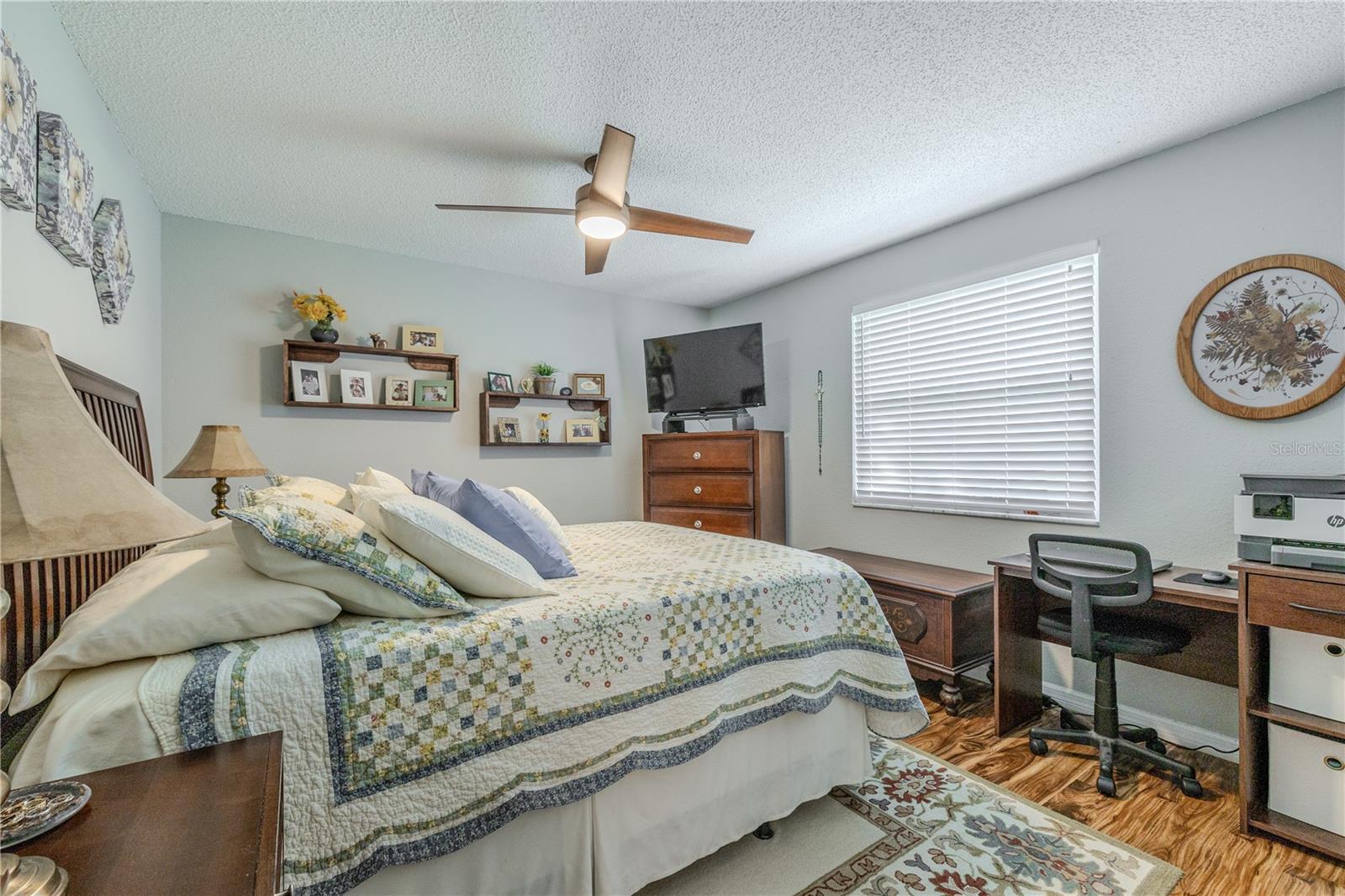 Bright and inviting bedroom 2 featuring warm wood flooring, a ceiling fan with integrated light, and ample wall space for flexible furniture placement within the split-bedroom layout.