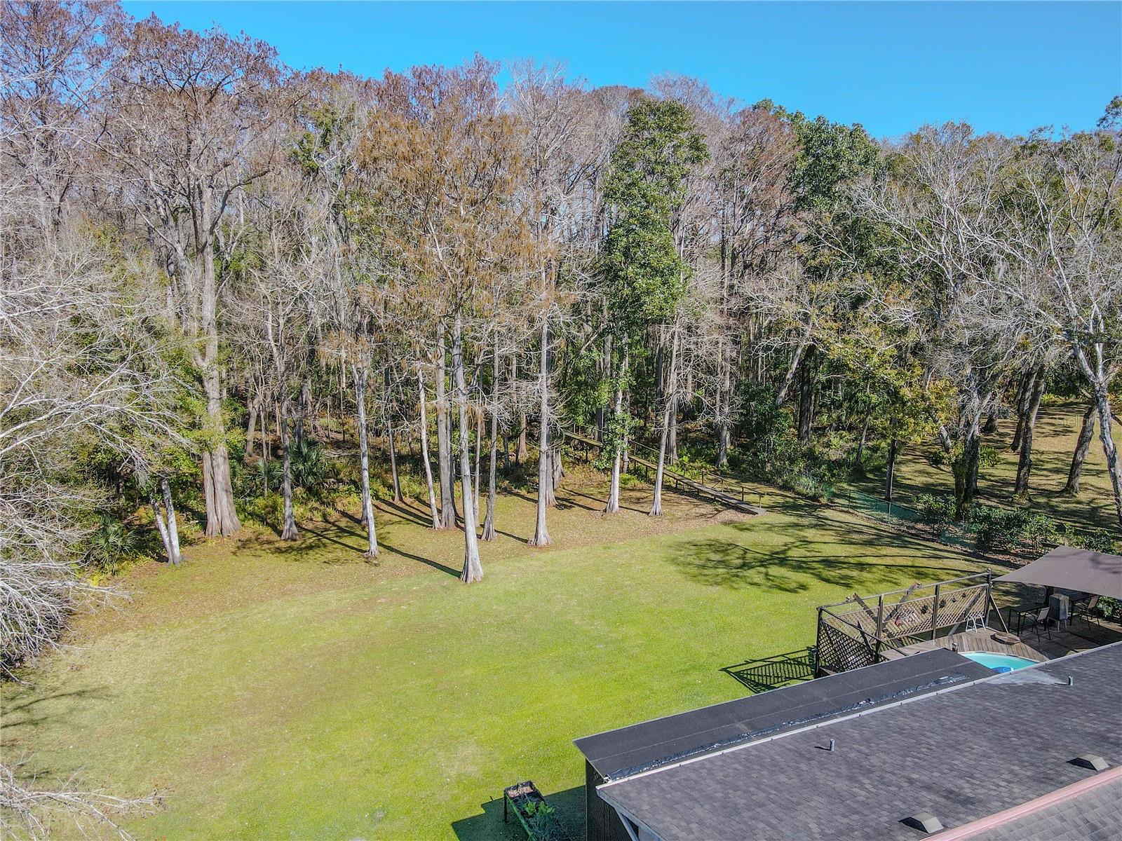 The backyard opens gracefully into a wooded landscape, where mature trees provide a serene, natural boundary beyond the maintained lawn.
