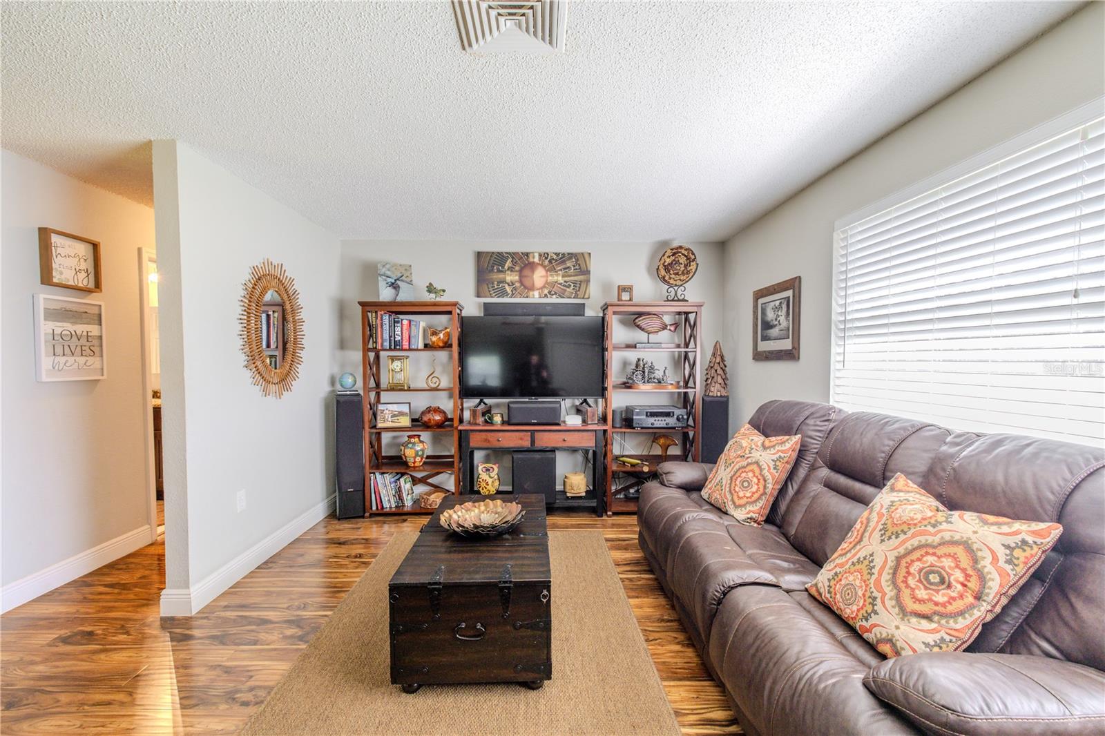 Comfortable living area with laminate floors, neutral wall tones, and a large window that fills the room with natural light.