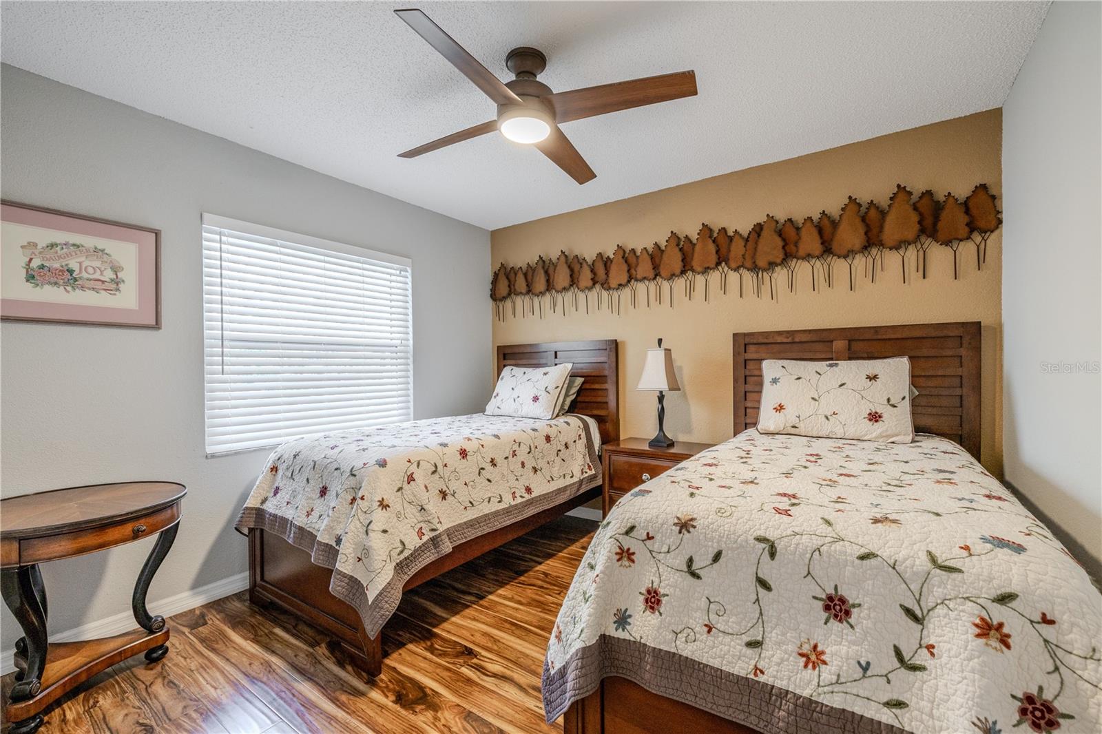 Well-sized third bedroom featuring twin-bed flexibility, wood flooring, a ceiling fan, and soft natural light, making it ideal for guests, family, or a dedicated workspace