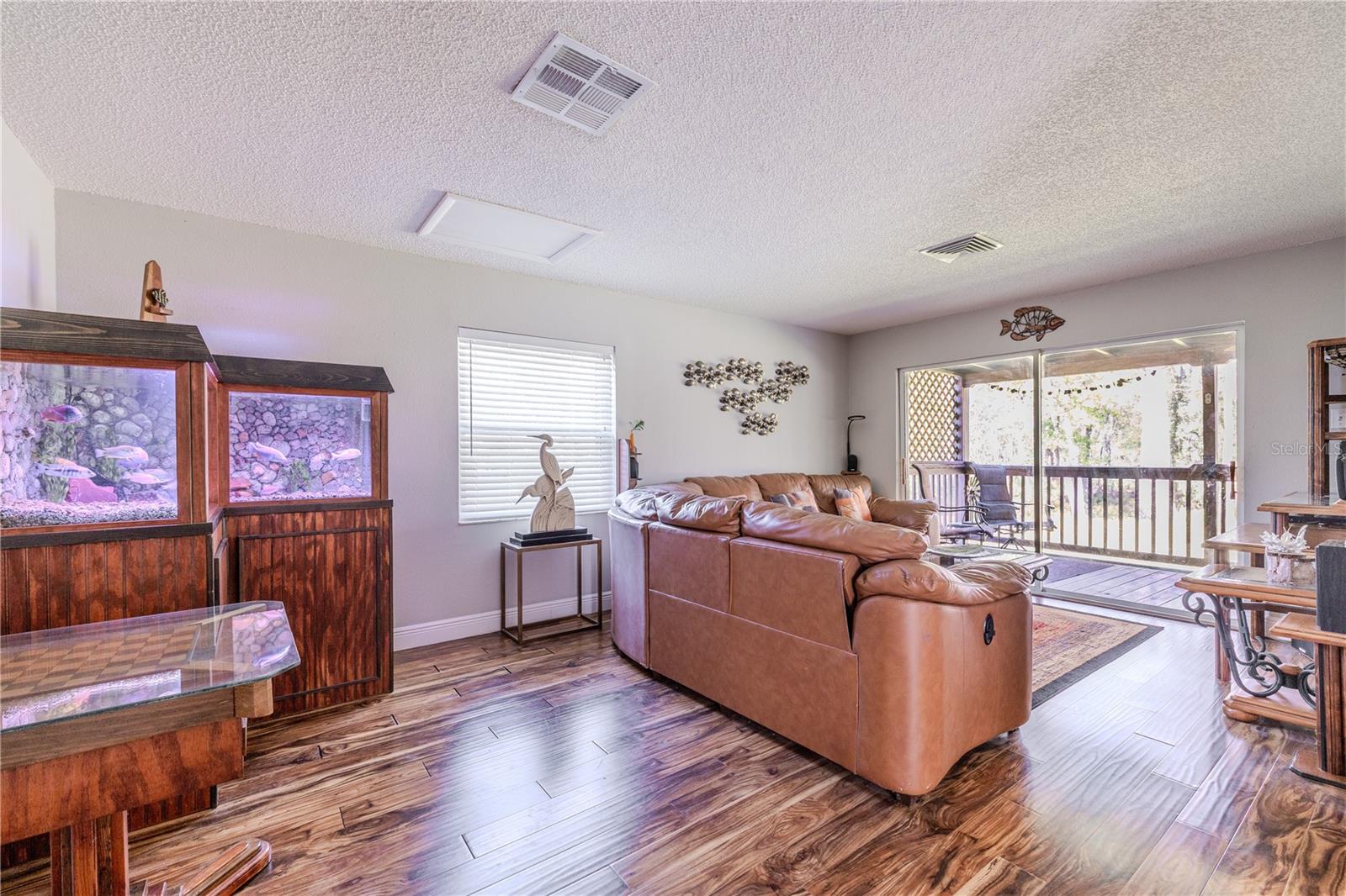 Spacious family room anchored by rich laminate flooring and a generous seating area positioned to take advantage of natural light. Sliding glass doors open directly to the covered deck, visually extending the living space outdoors and offering peaceful views of the surrounding trees.