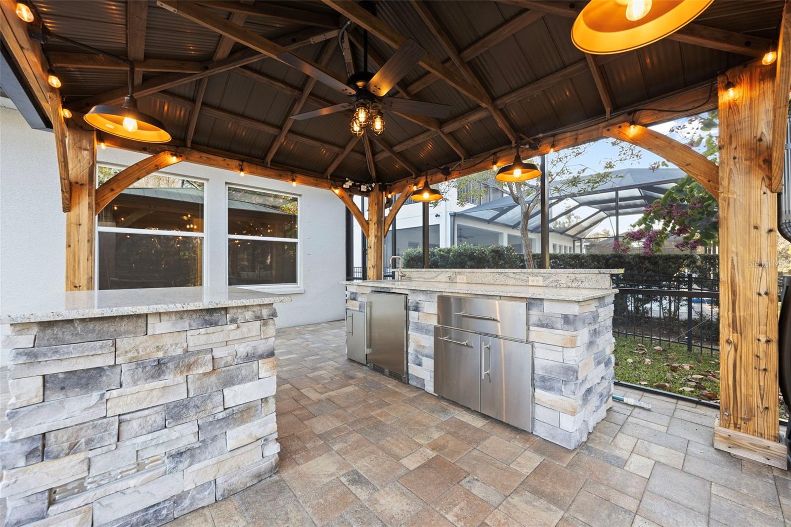 Outdoor kitchen with stone & granite countertops, fridge, sink and storage.