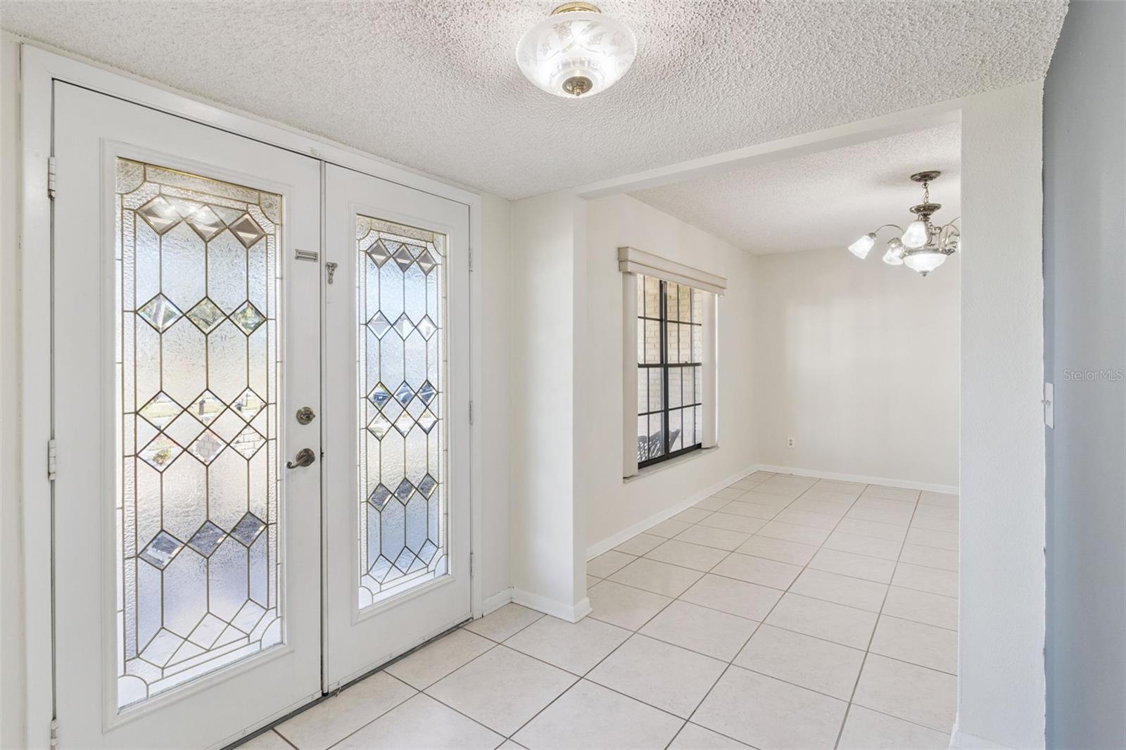 View from the front entry featuring decorative glass double doors. The tile flooring leads directly into the formal dining room, visible through a wide interior opening.