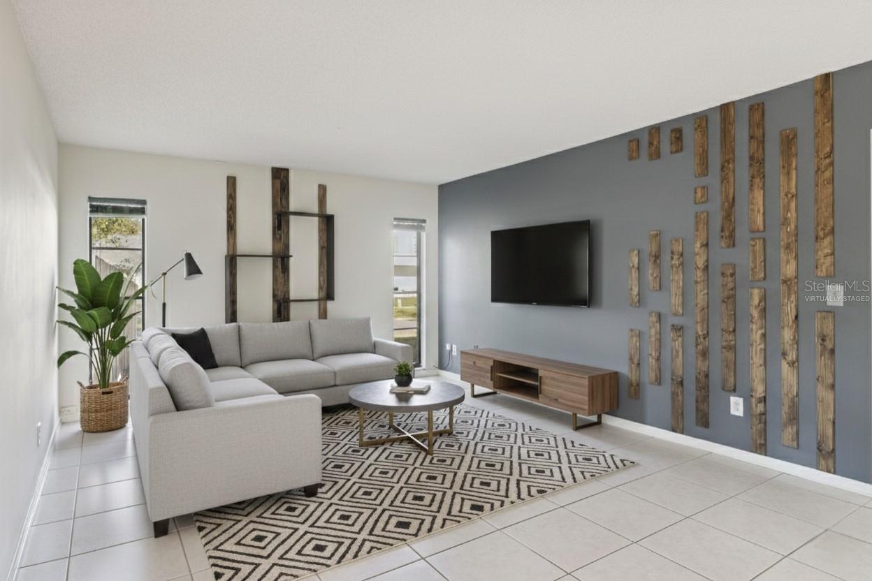 This photo is virtually staged. Family room featuring tile flooring, neutral wall colors, and a decorative accent wall. The room is virtually staged with a sectional sofa, media console, area rug, and wall-mounted television to demonstrate layout possibilities.