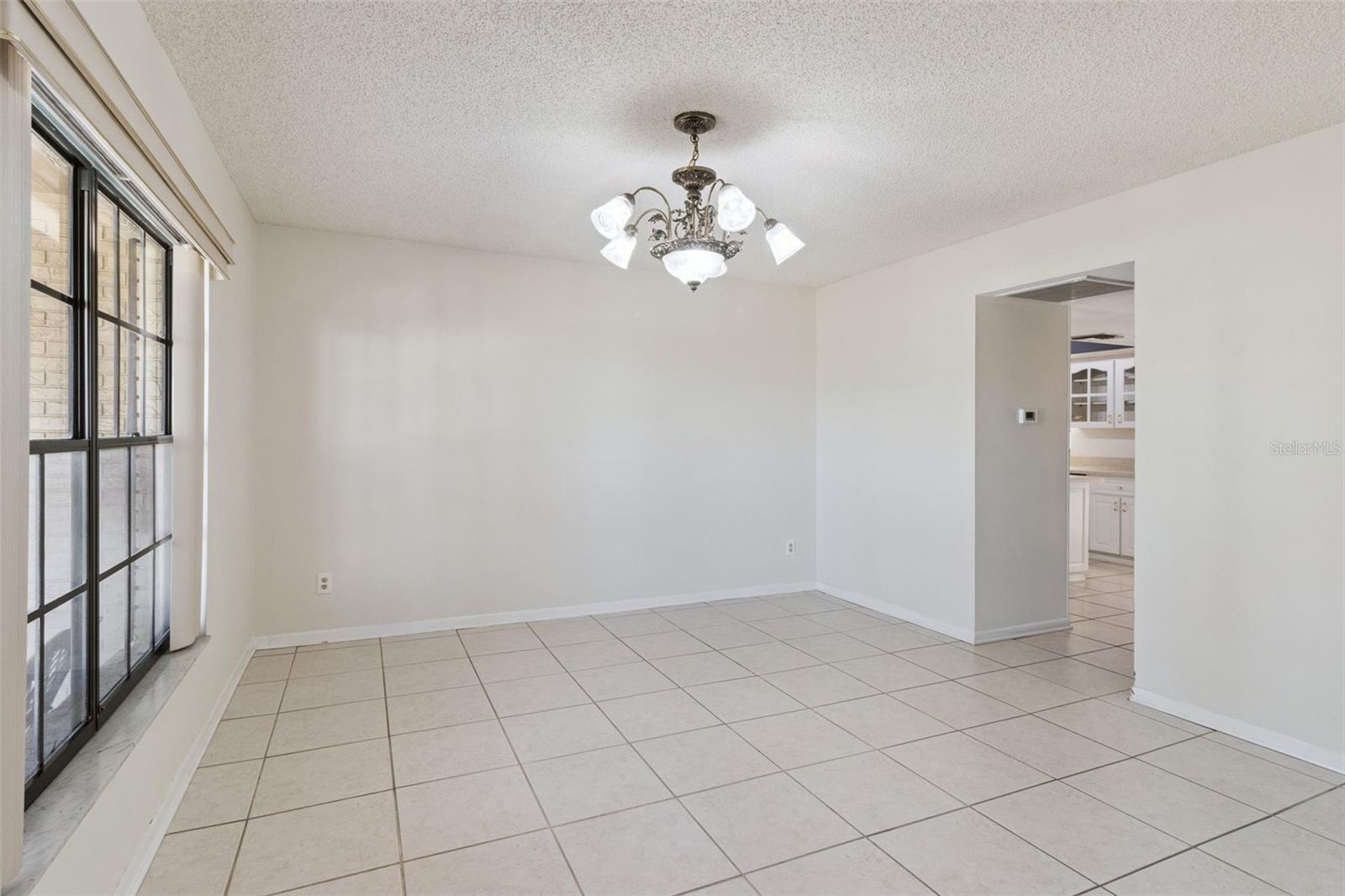 Alternate view of the formal dining room highlighting the chandelier, tile flooring, and open connection to the kitchen area through a wide doorway.