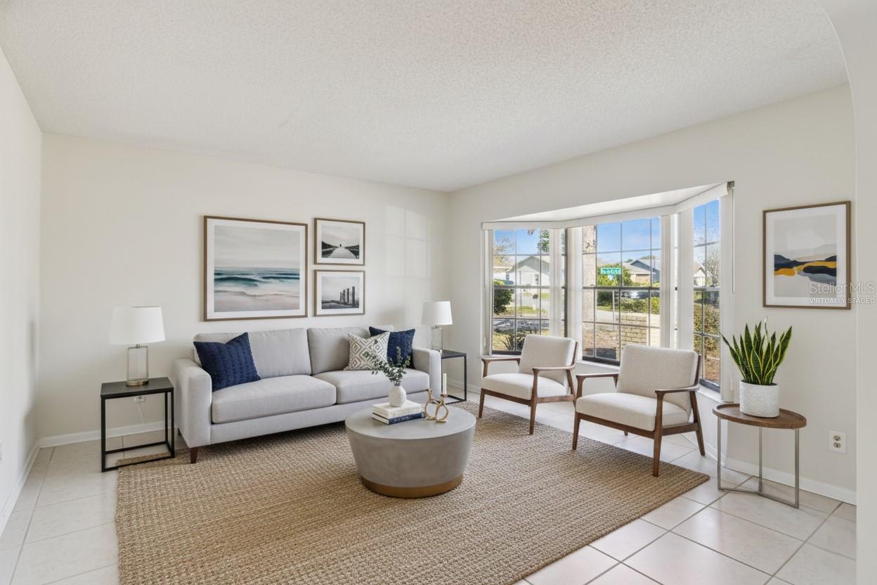 This photo is virtually staged. Formal living room with tile flooring, neutral walls, and a bay-style window area that brings in natural light. The space is virtually staged with seating, an area rug, and accent furniture to illustrate one possible arrangement.