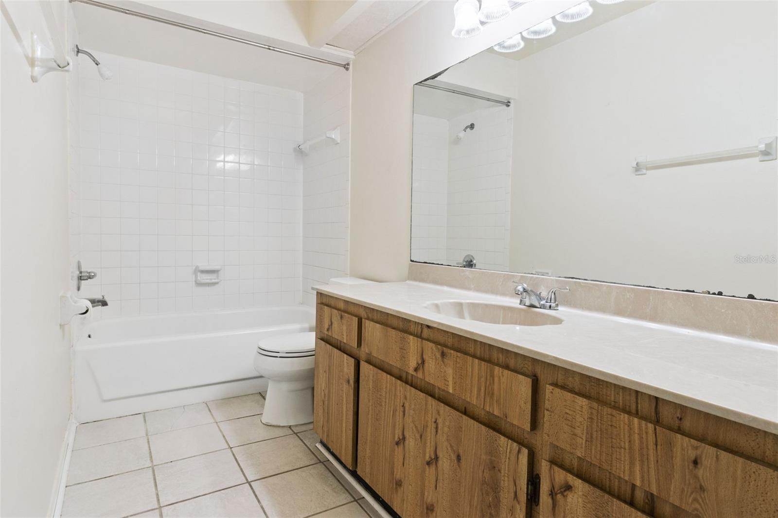 Second-floor guest bathroom with a tub/shower combination, single-sink vanity, and toilet. Tile flooring and a wide vanity mirror enhance the clean, functional layout.