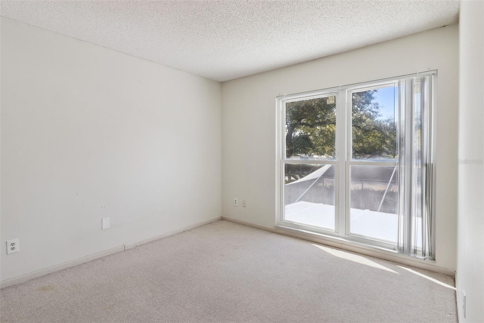 Second-floor bedroom located across the hall from the primary bedroom, facing the rear of the home. The room features carpeted flooring, a window, and neutral finishes.
