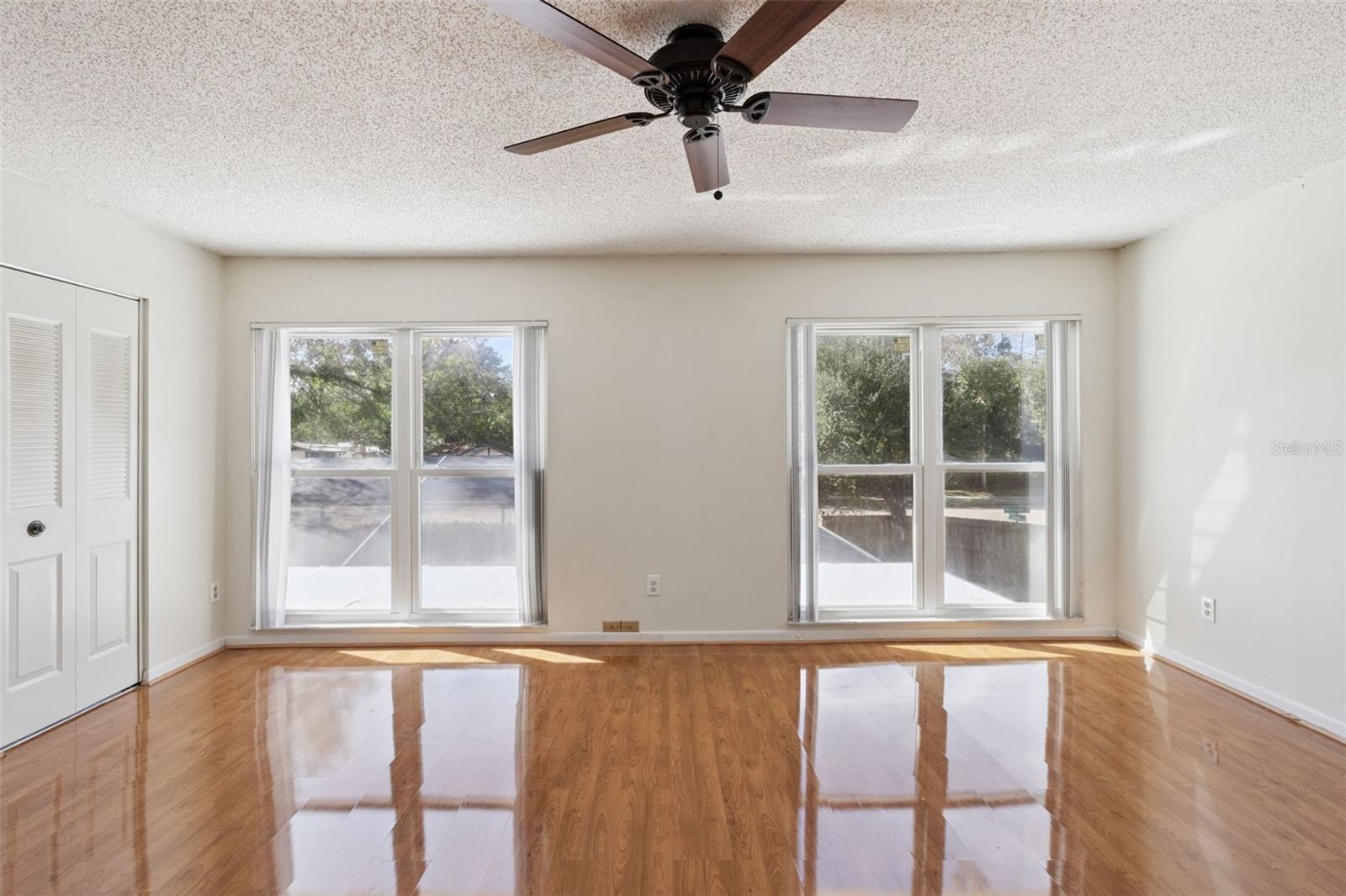 Alternate view of the primary bedroom showcasing luxury vinyl plank flooring, neutral walls, and multiple windows that provide a bright, airy atmosphere.