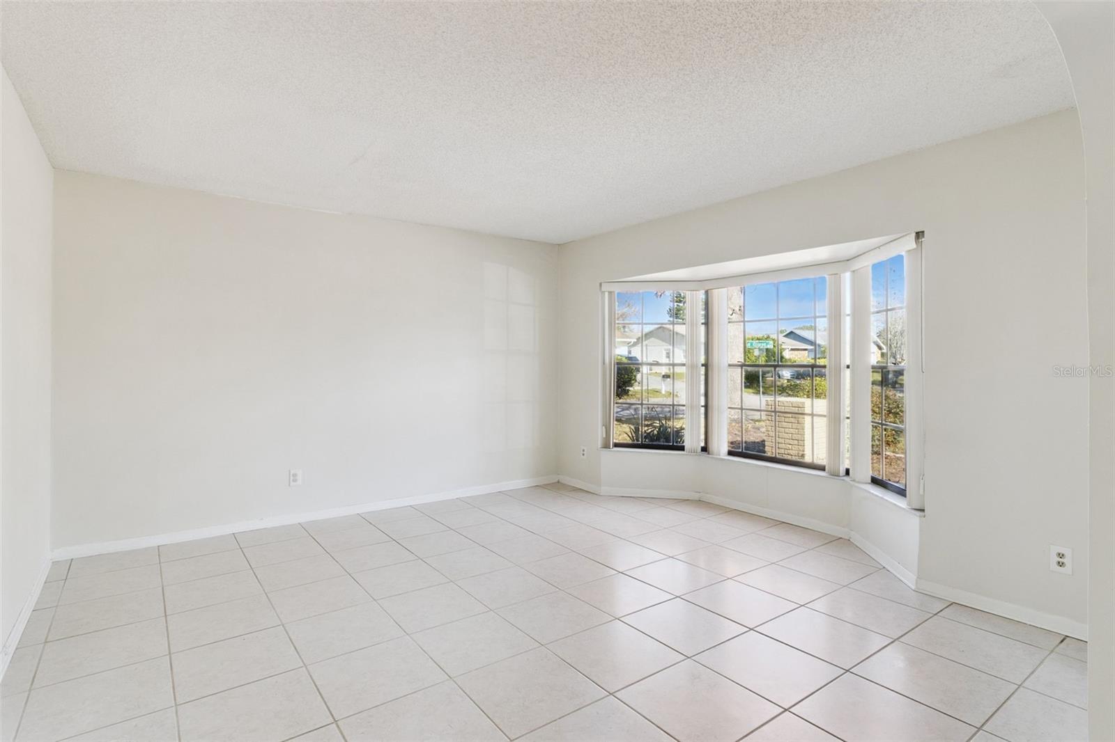 Formal living room with tile flooring, neutral walls, and a large bay window that brings in natural light. The open layout provides flexibility for seating or a sitting area.