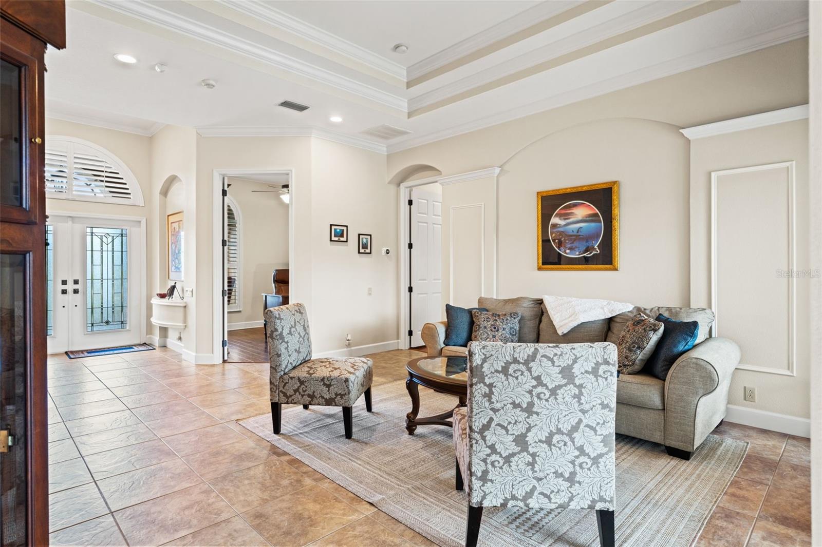 A spacious seating arrangement centered around a glass-top coffee table creates a comfortable setting for gatherings, highlighted by detailed millwork and high ceilings.