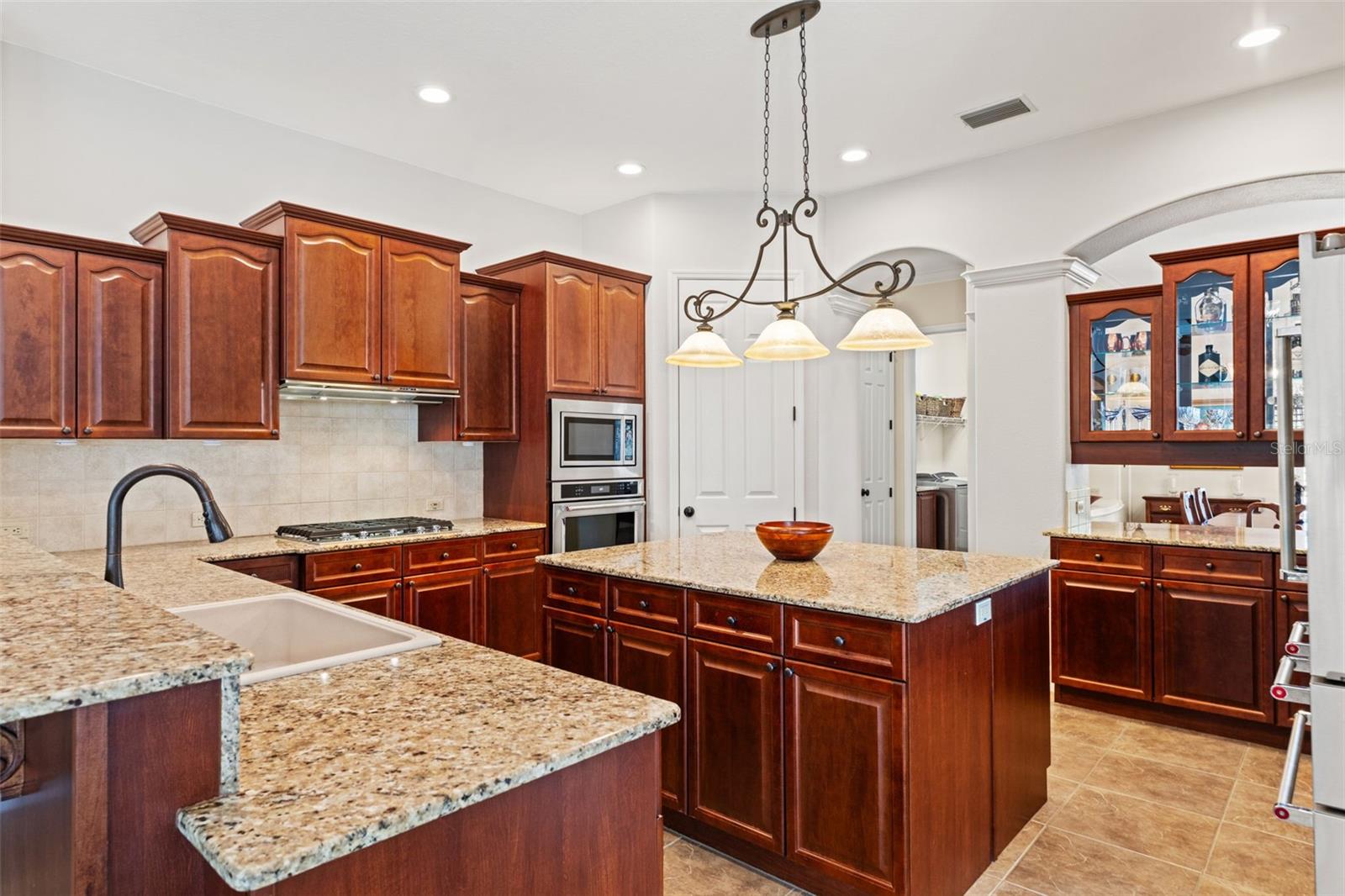 This spacious kitchen showcases rich wood cabinetry, granite countertops, a center island, and ample prep space, all illuminated by stylish pendant lighting.