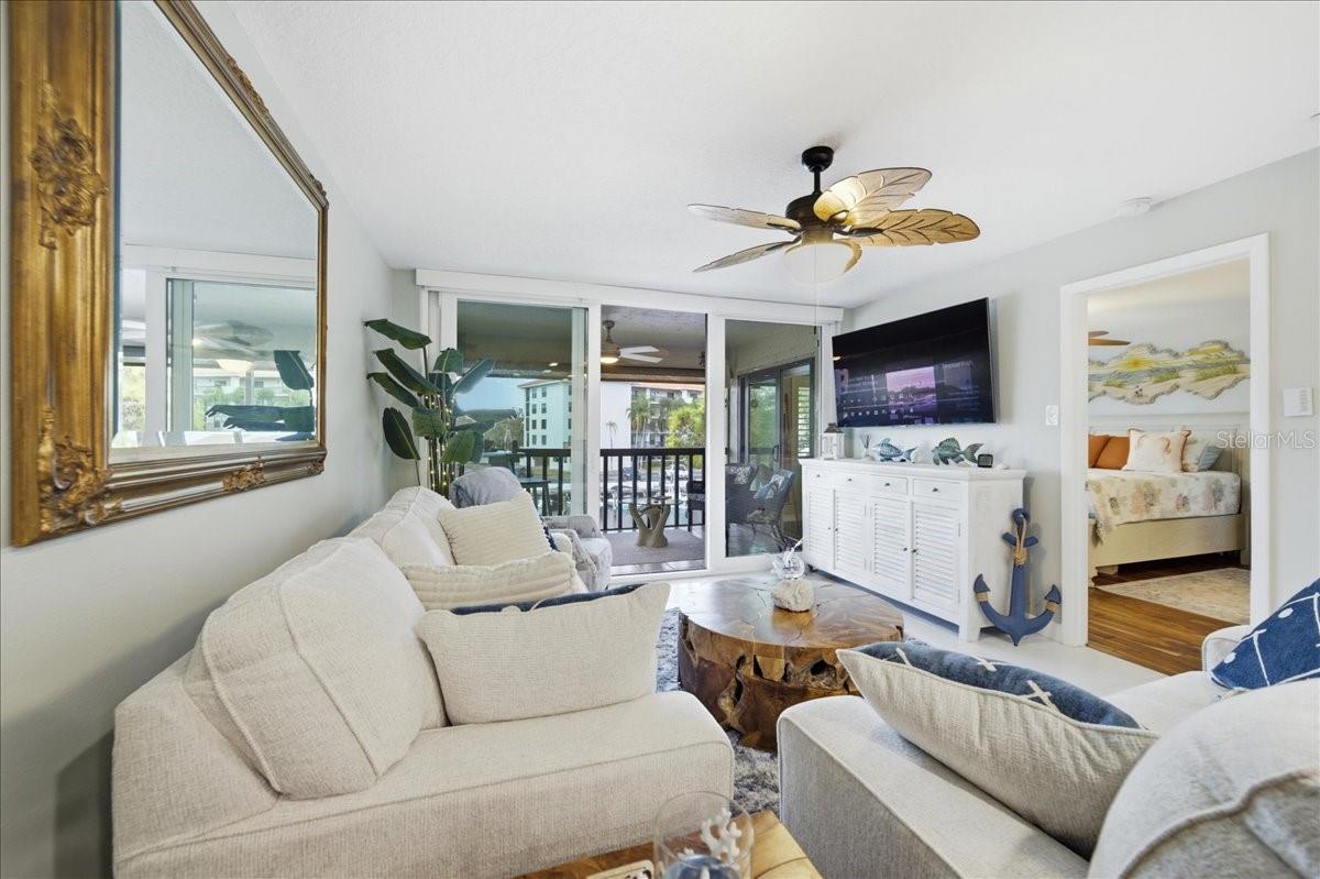 Living room is a relaxing space to gather and unwind with gorgeous easy-maintenance tile floors a decorative ceiling fan and peaceful views out the wall of glass sliders to the balcony.