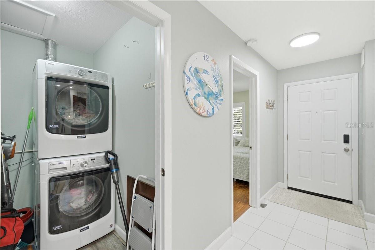 Walk-in Utility closet with stacked full-sized washer and dryer and storage space.