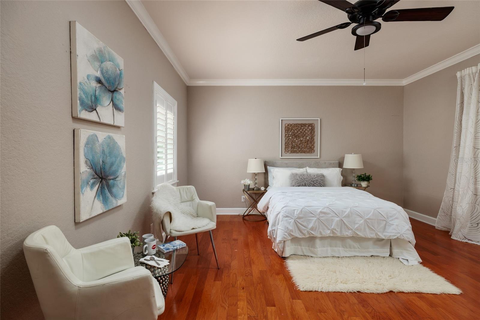 Primary Bedroom with hardwood floors, plantation shutters and crown molding.