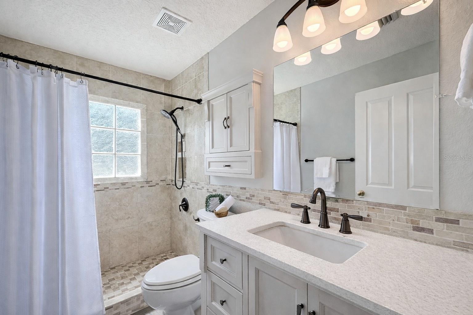 Large guest bathroom with walk in shower and new stone countertop.