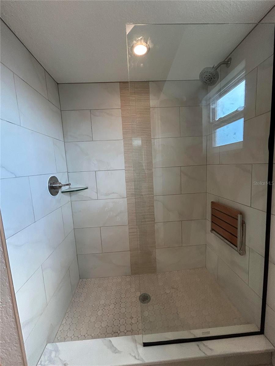 Bathroom shower with glass panel and foldable sitting chair