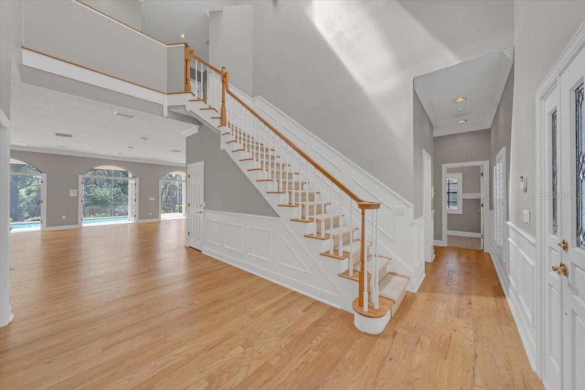 Dramatic two-story foyer showcases hardwood floors, elegant staircase, and sunlit open living areas.