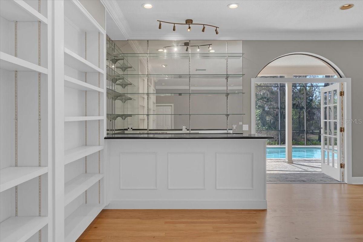 Custom built-in shelving and a sleek bar area open through French doors to the lanai.