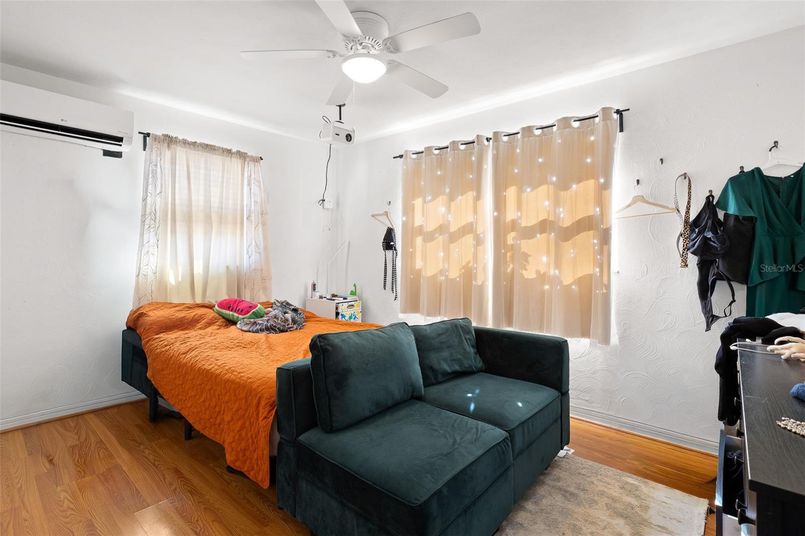 Primary bedroom is light and bright with multiple windows for natural light, complemented by wood-look flooring, a ceiling fan, and efficient mini-split A/C for year-round comfort.
