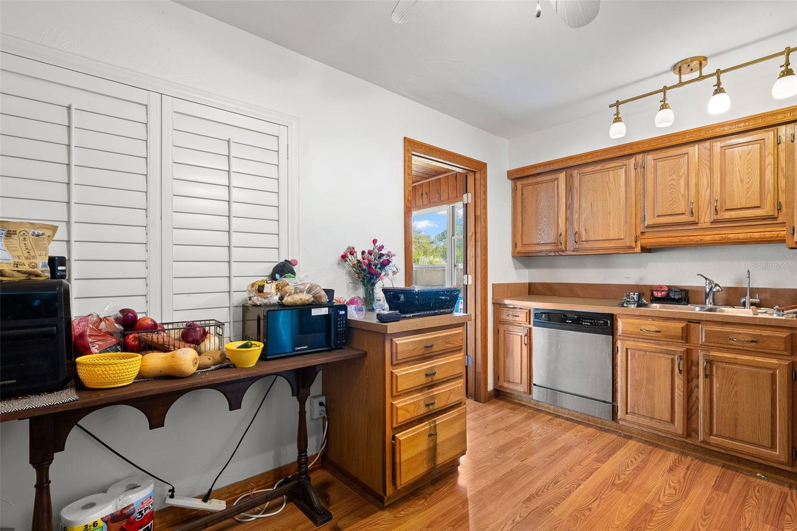 Functional kitchen with ample cabinetry and generous counter space complemented by a brushed brass multi-light fixture, Plantation shutters, and a layout that connects easily to adjacent living areas and outdoor access.