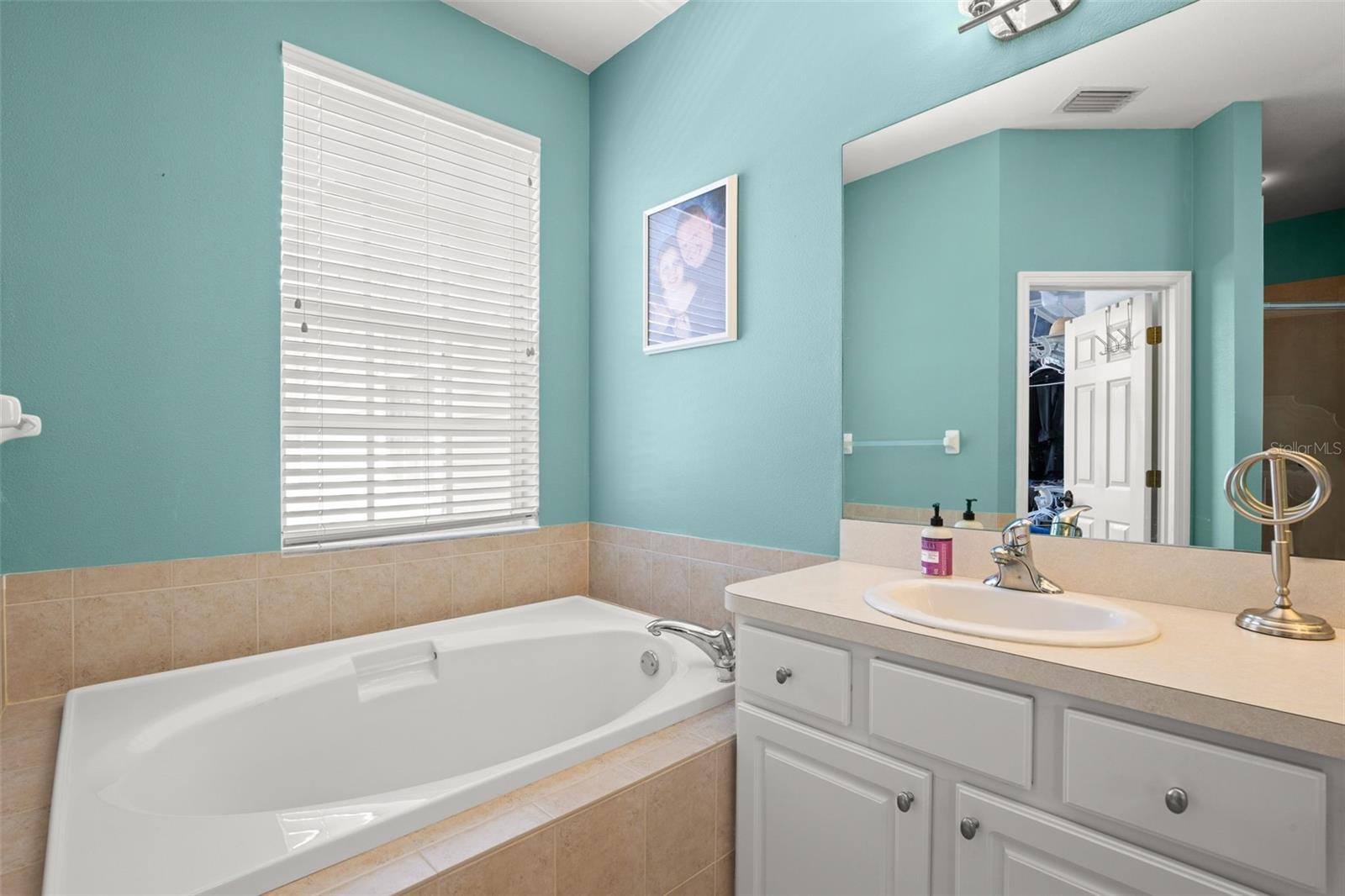 Primary ensuite featuring a soaking tub set beneath a window, tile surround, and an adjacent vanity with ample counter space, all complemented by natural light.