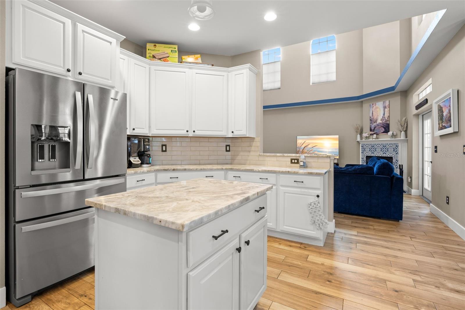 Open-concept kitchen with marble countertops, center island, stainless steel appliances, and alabaster cabinetry, flowing effortlessly into the light-filled living space with soaring ceilings.