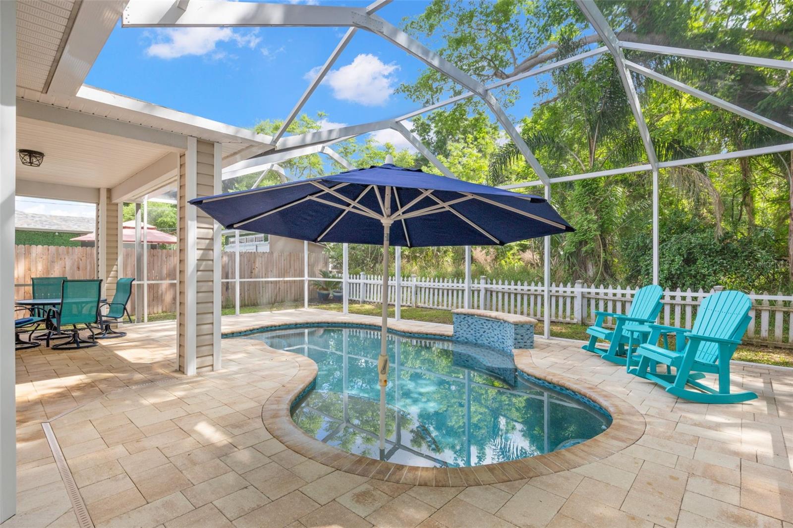 Tile saltwater pool with sun shelf and umbrella, surrounded by a stone paver deck.
