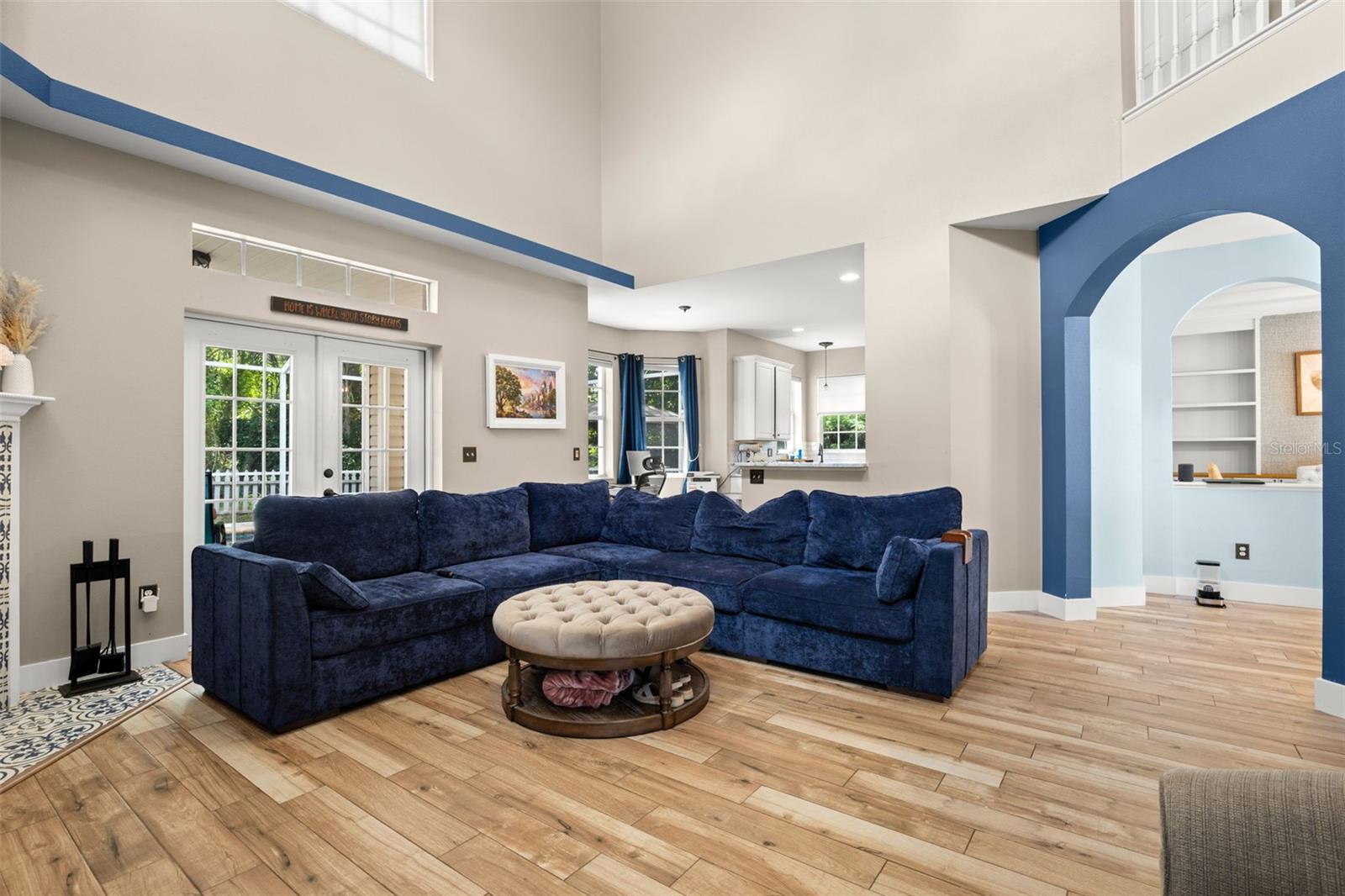 Expansive living room with soaring ceilings, wood plank flooring, French doors to the lanai, and arched architectural details, filled with natural light.