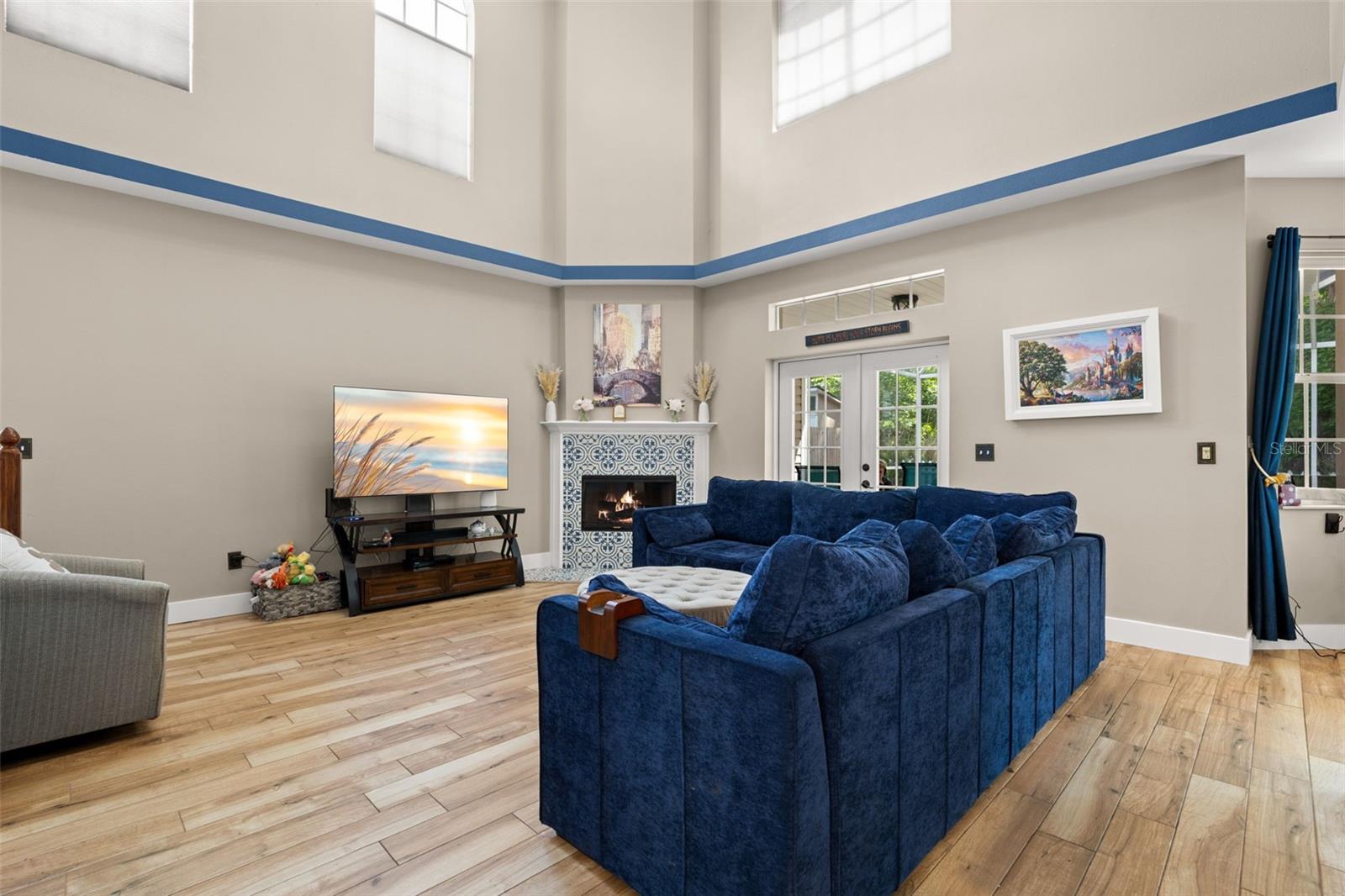 Spacious living room showcasing soaring ceilings, clerestory windows, and wood plank flooring, centered around a mosaic tile wood-burning fireplace with mantle.