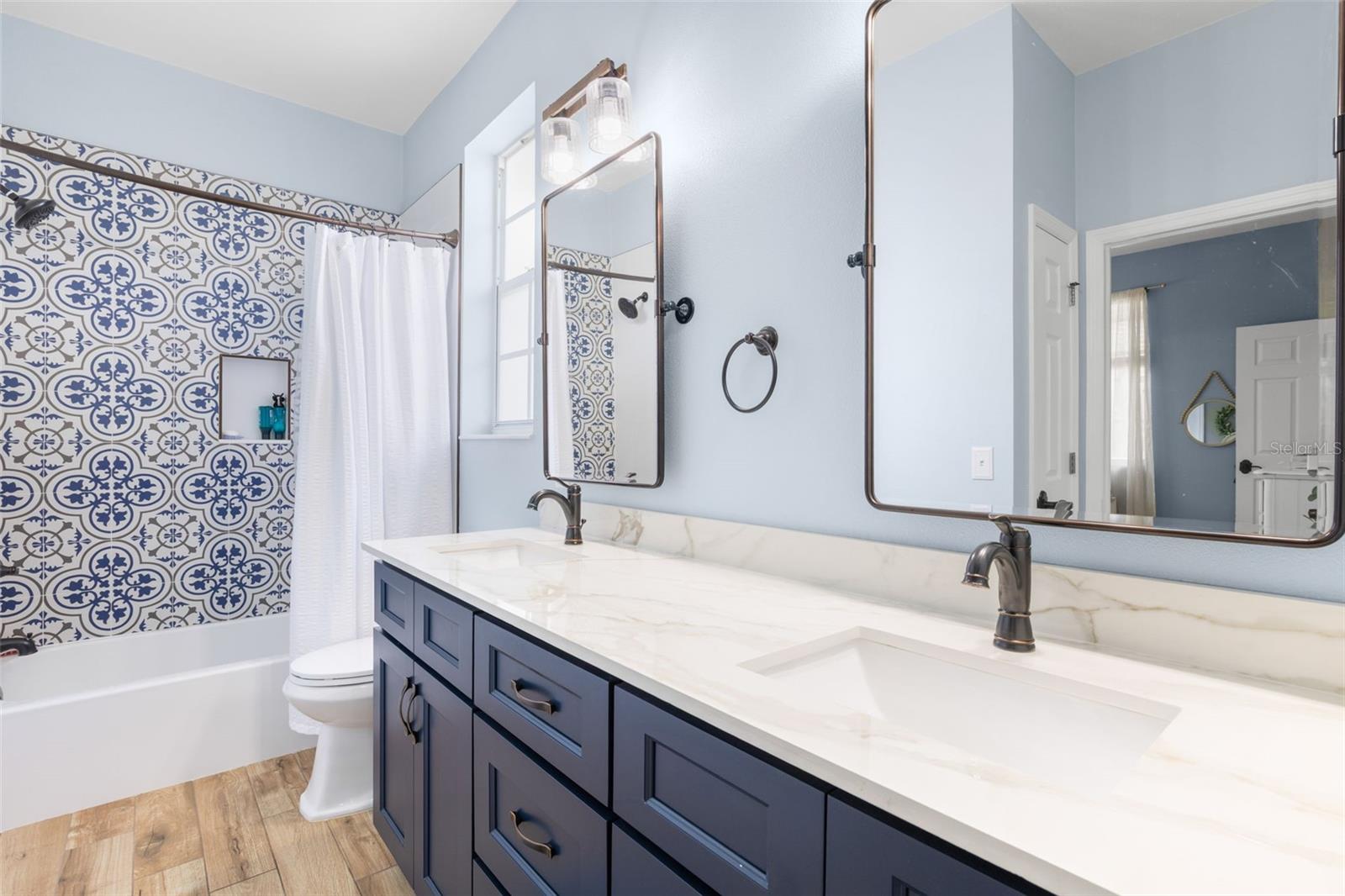 Upstairs Jack and Jill bathroom featuring a dual-sink vanity with quartz countertops, navy cabinetry, and a tub/shower combination accented by decorative tile.
