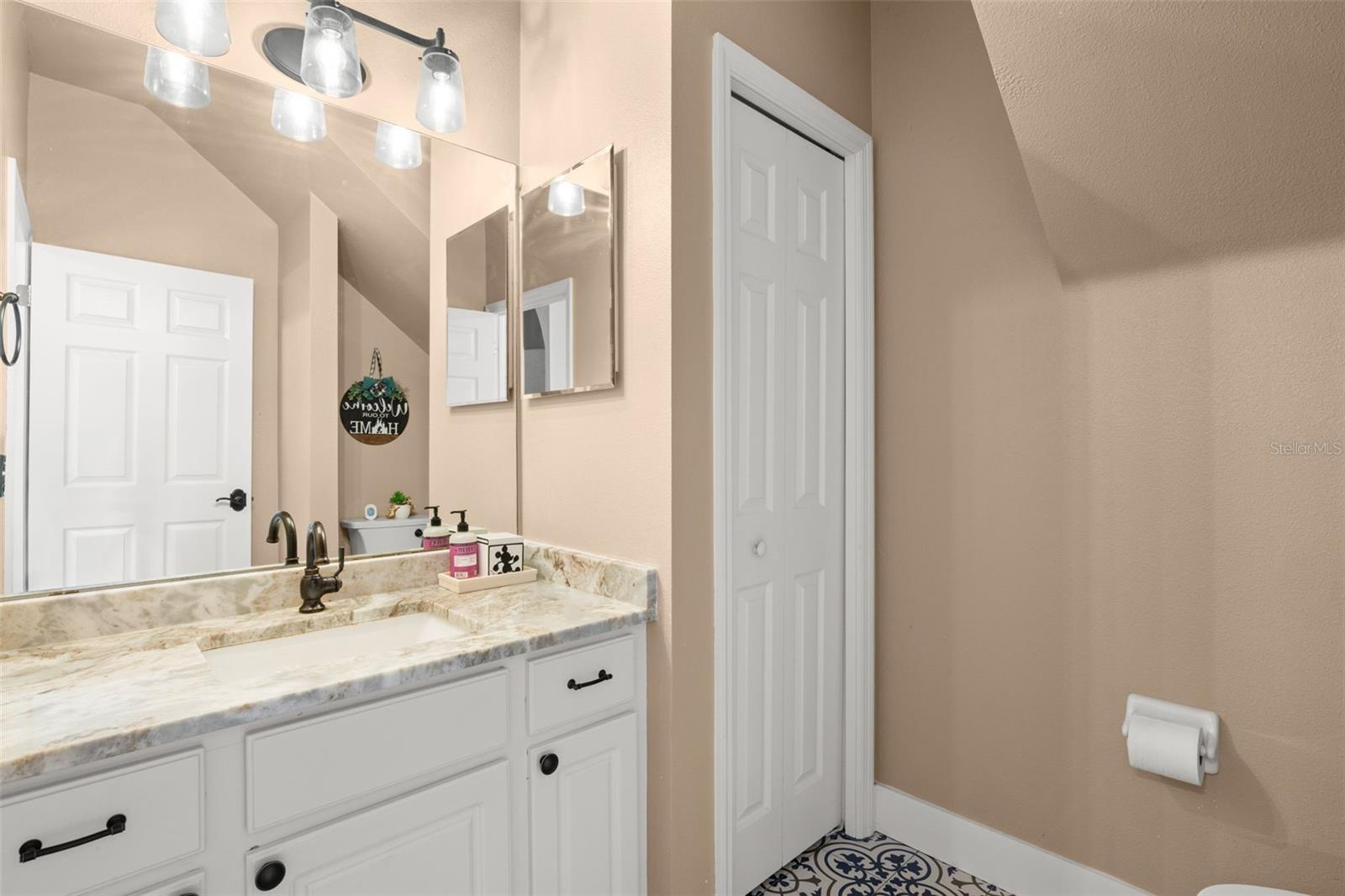 A well-appointed half bath features a marble countertop vanity, mosaic tile flooring, and a linen closet.