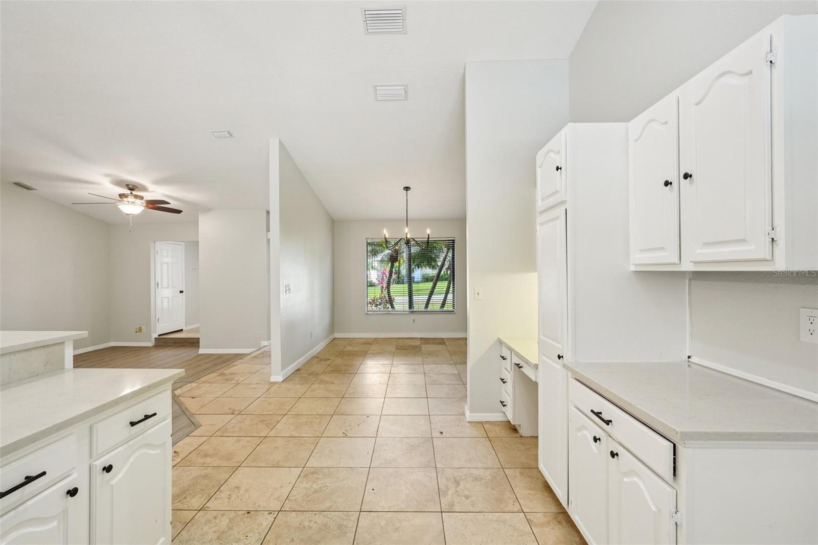 The spacious kitchen is well-equipped with quartz countertops, a tile backsplash, ample bright white cabinetry, stylish open wood shelving, a built-in desk, and stainless-steel appliances, including a new refrigerator. The breakfast bar, accented with charming shiplap detail, provides a comfortable spot for casual meals or morning coffee while naturally connecting to the family room.