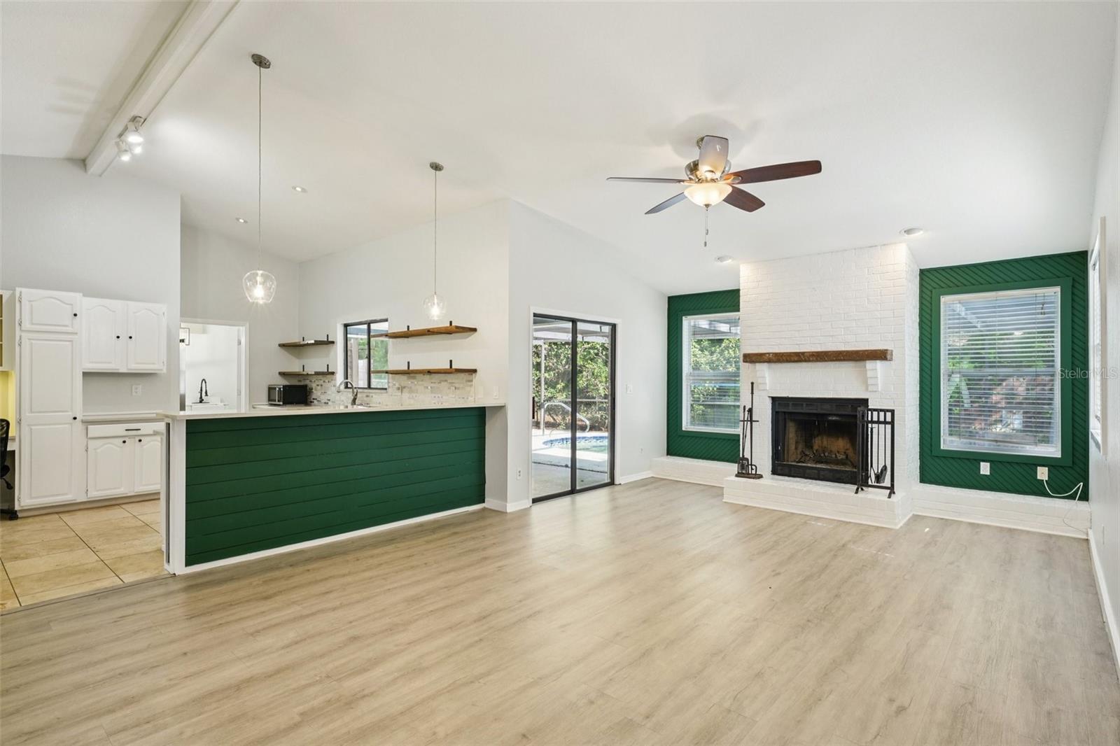 The family room features vaulted ceilings, a wood-burning fireplace with hearth and mantle, and an energy-efficient solar tube skylight that fills the space with natural, diffused light. Sliding glass doors lead to the covered patio and screened-in pool area, extending the living space outdoors.