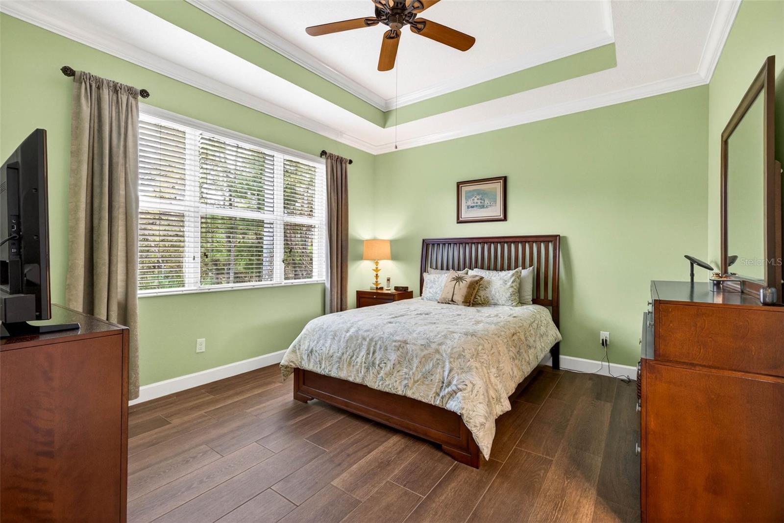Primary bedroom with large picture window overlooking the Little Manatee River State Park. Tray ceiling with crown molding, ceiling fan and window treatments.