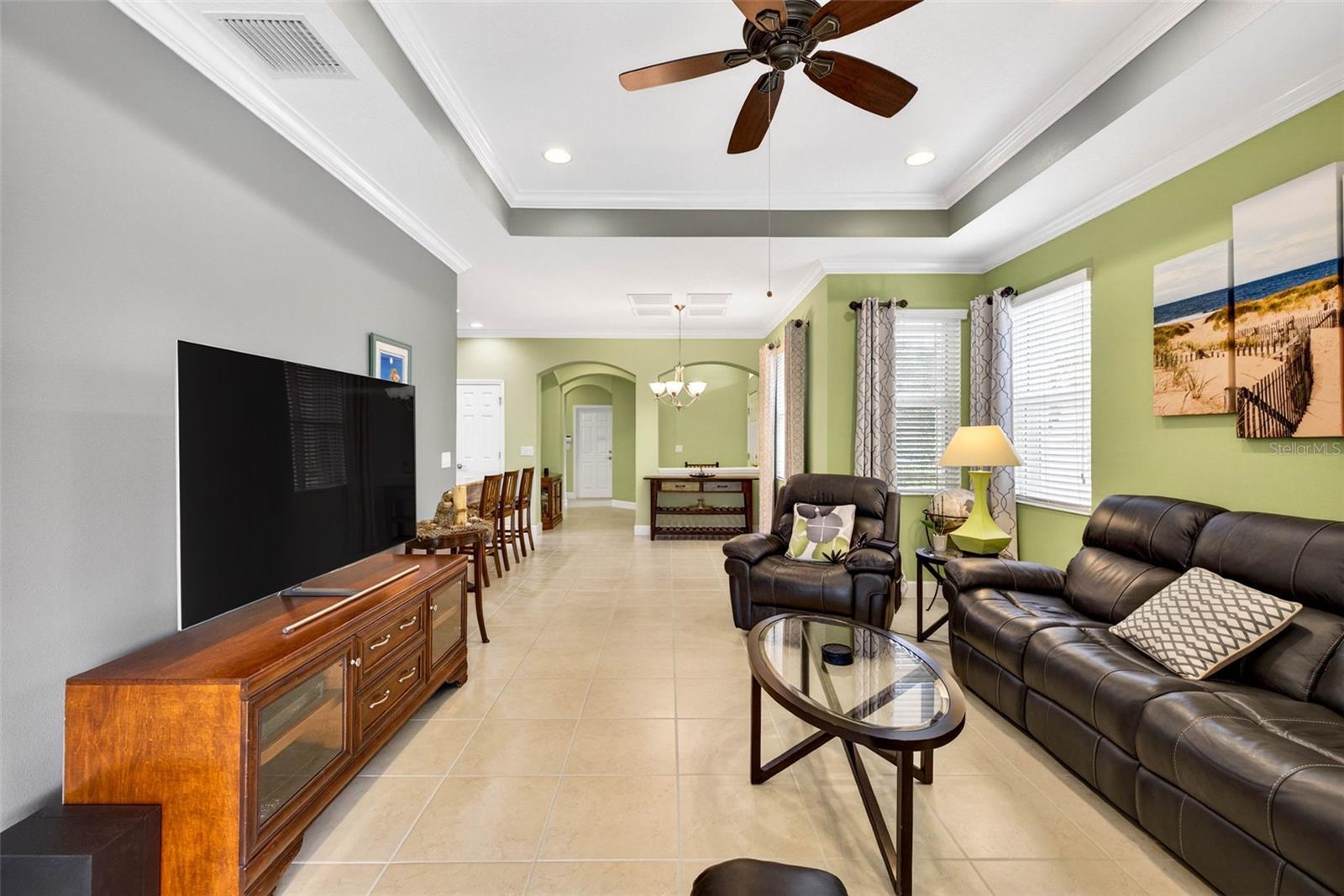 Living room and dining room combined space with tile and crown molding throughout. Window treatments convey